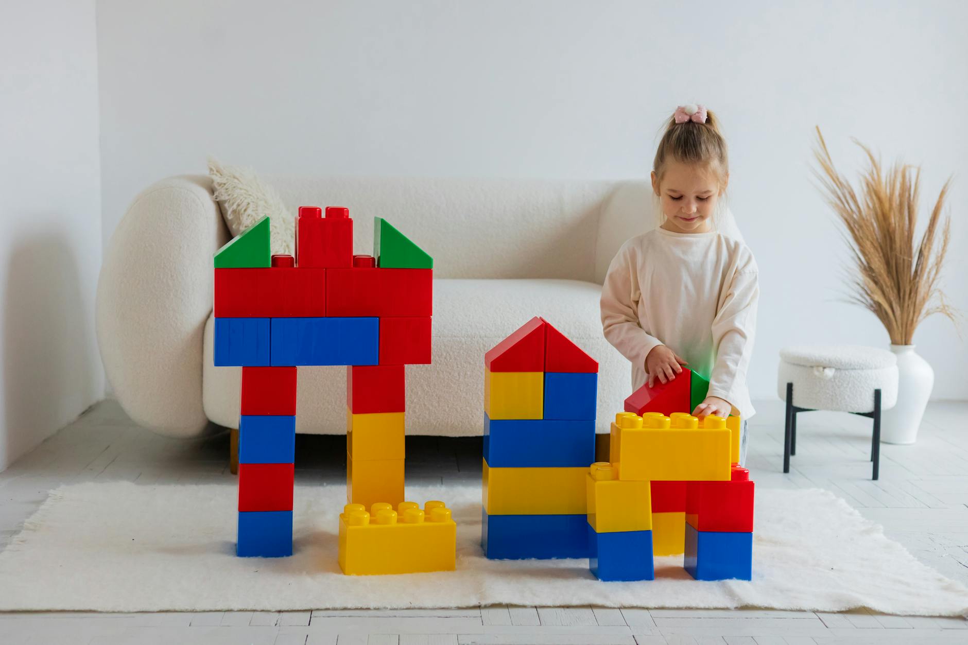A young girl building structures with large, colorful blocks in a cozy living room setting. - child developmental milestones