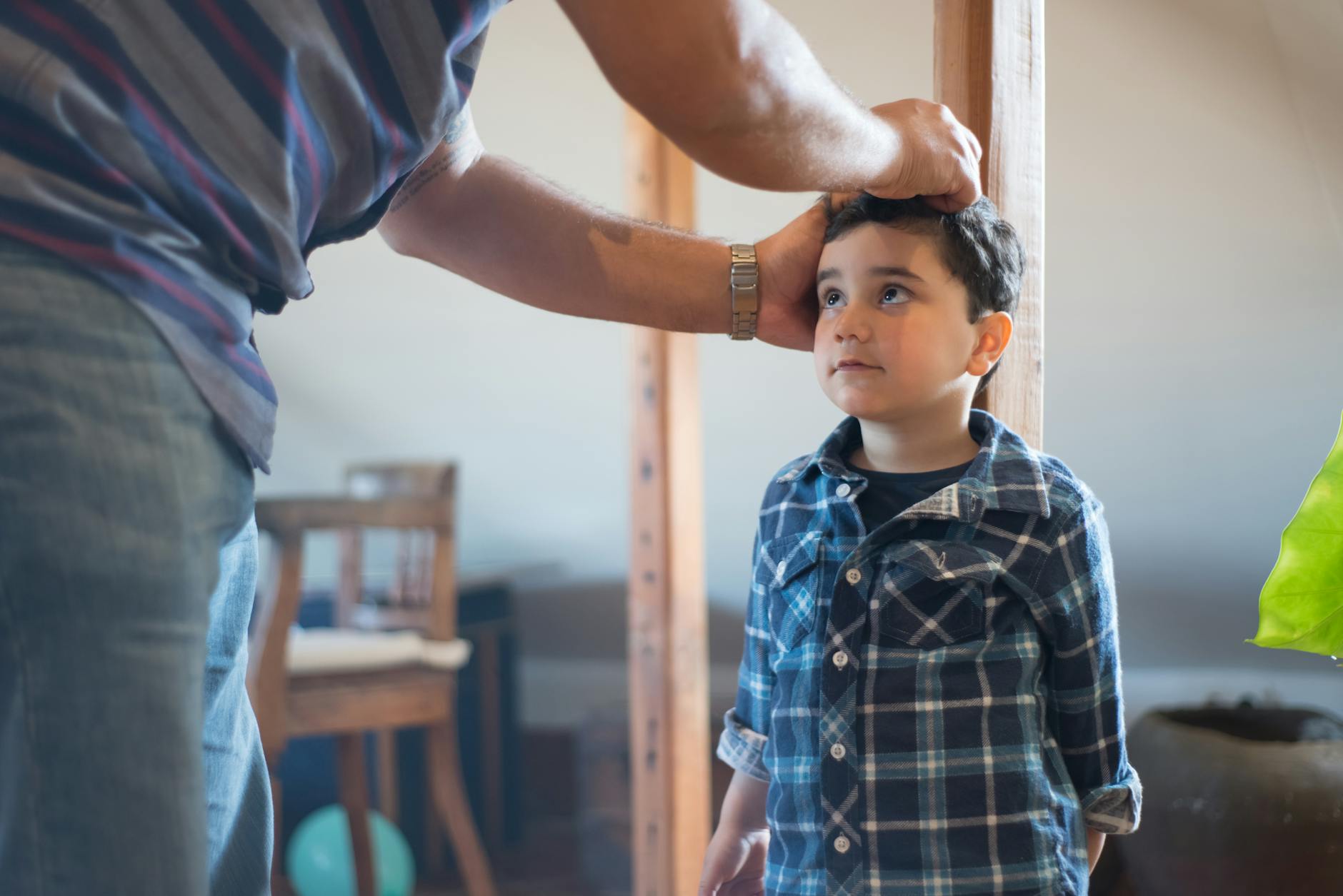 A father marking his young son's height on a wooden pole indoors, capturing a family bonding moment. - child growth spurts