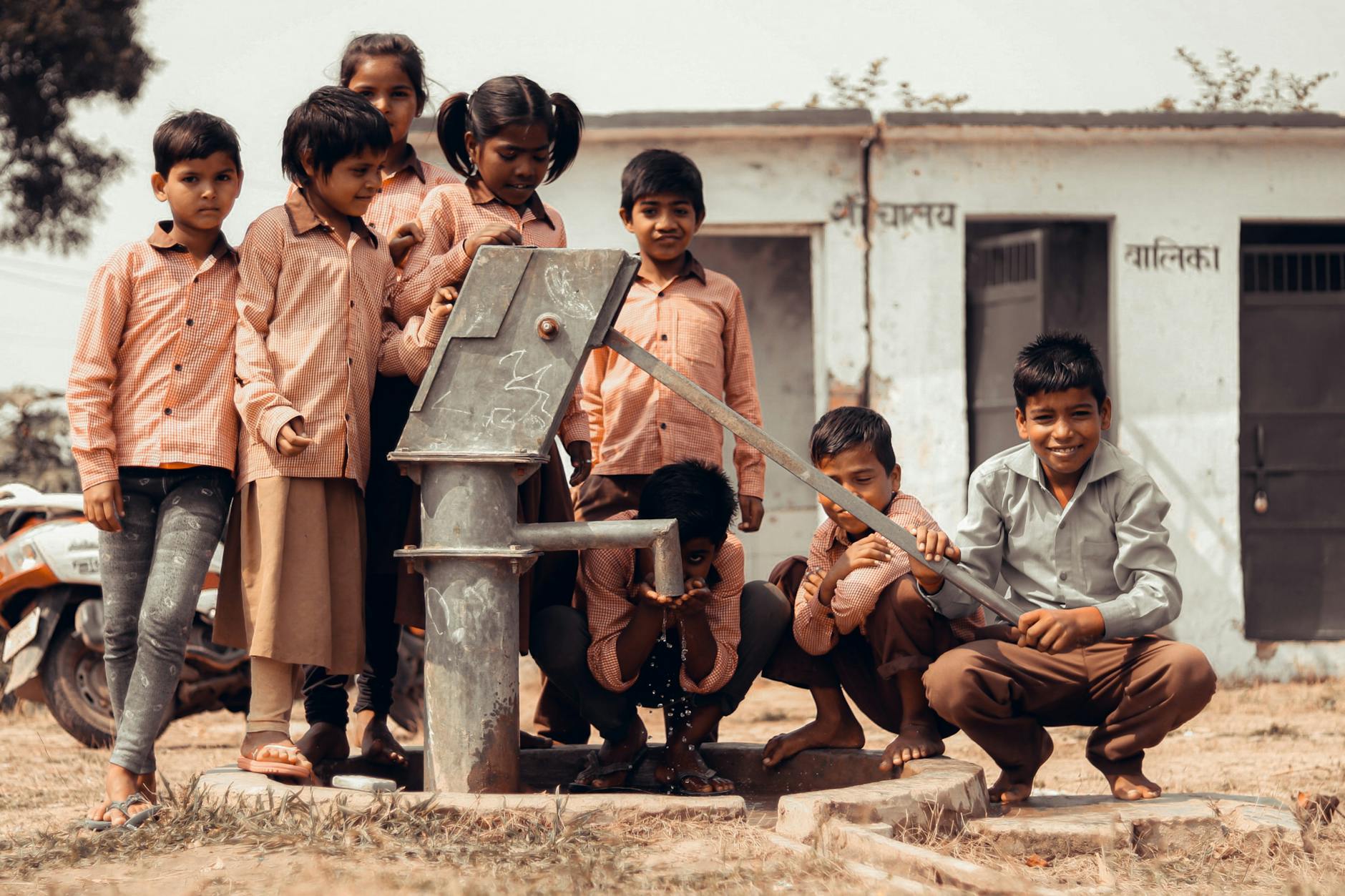 A group of Indian children gather joyfully around a manual water pump outdoors. - childhood meltdowns