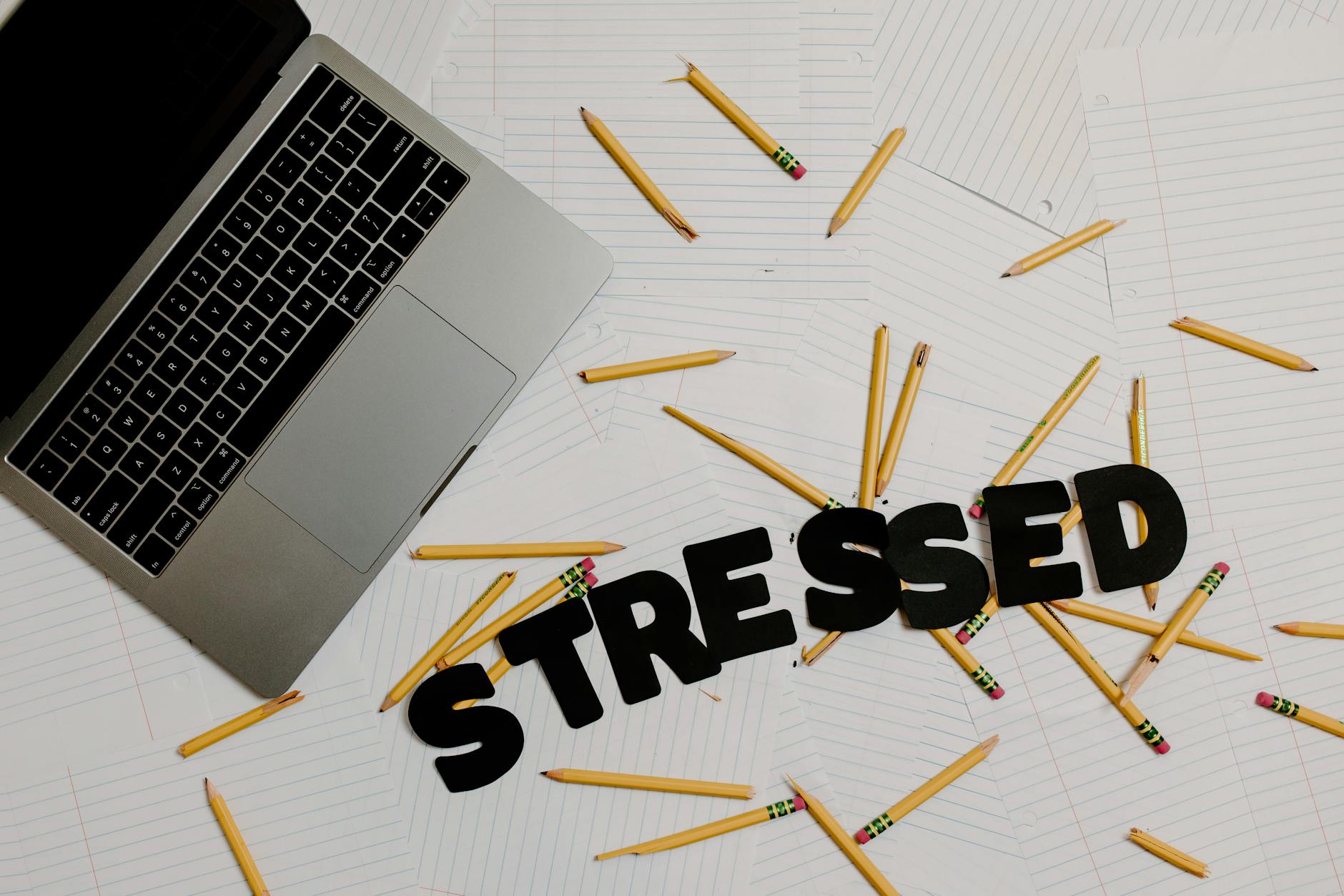 Image of a cluttered desk with laptop and scattered pencils spelling 'stressed,' symbolizing burnout and overwork. - clear mental clutter