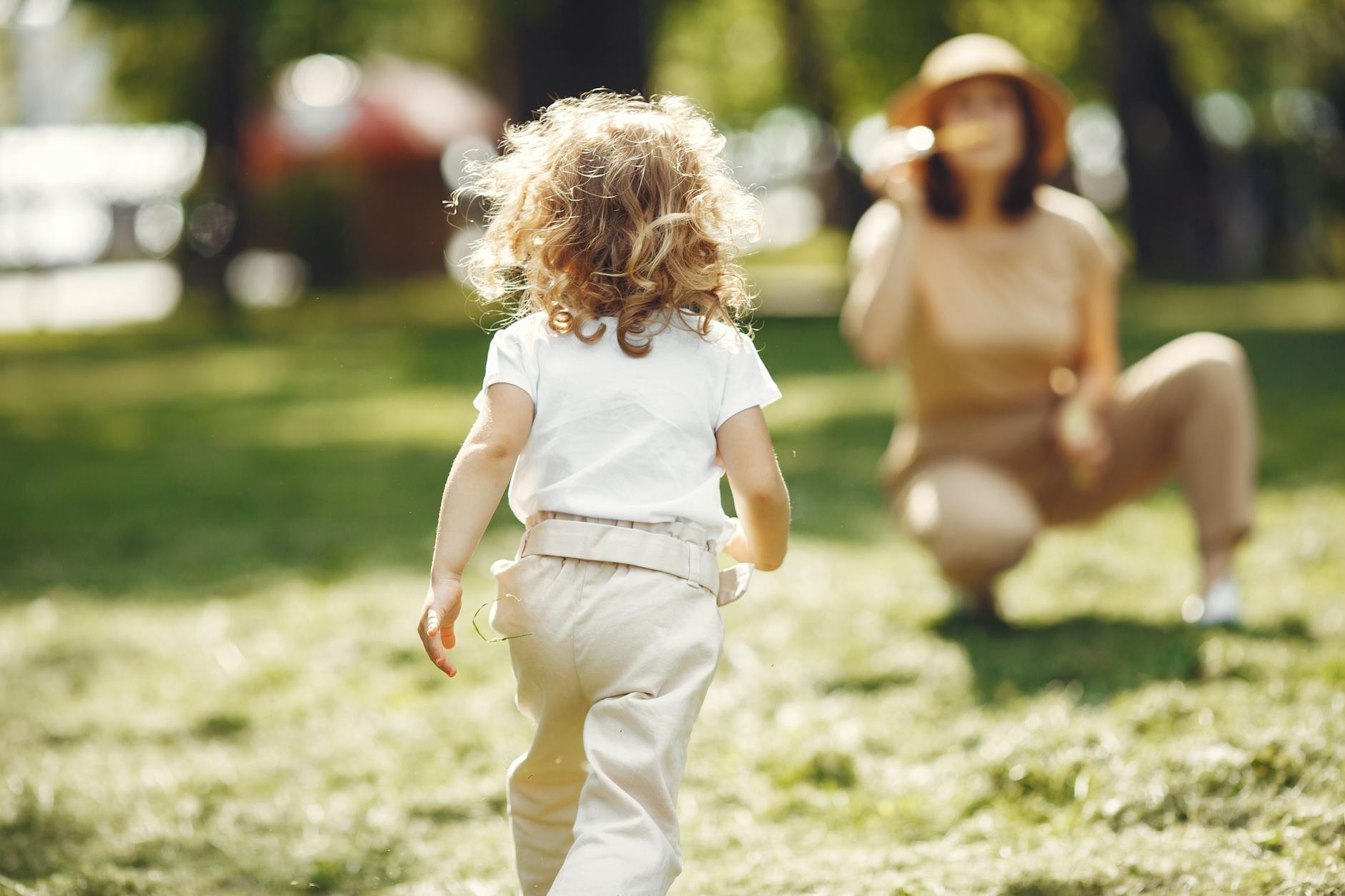 A mother crouches while her child runs towards her in a sunny park. - co-parenting spring break