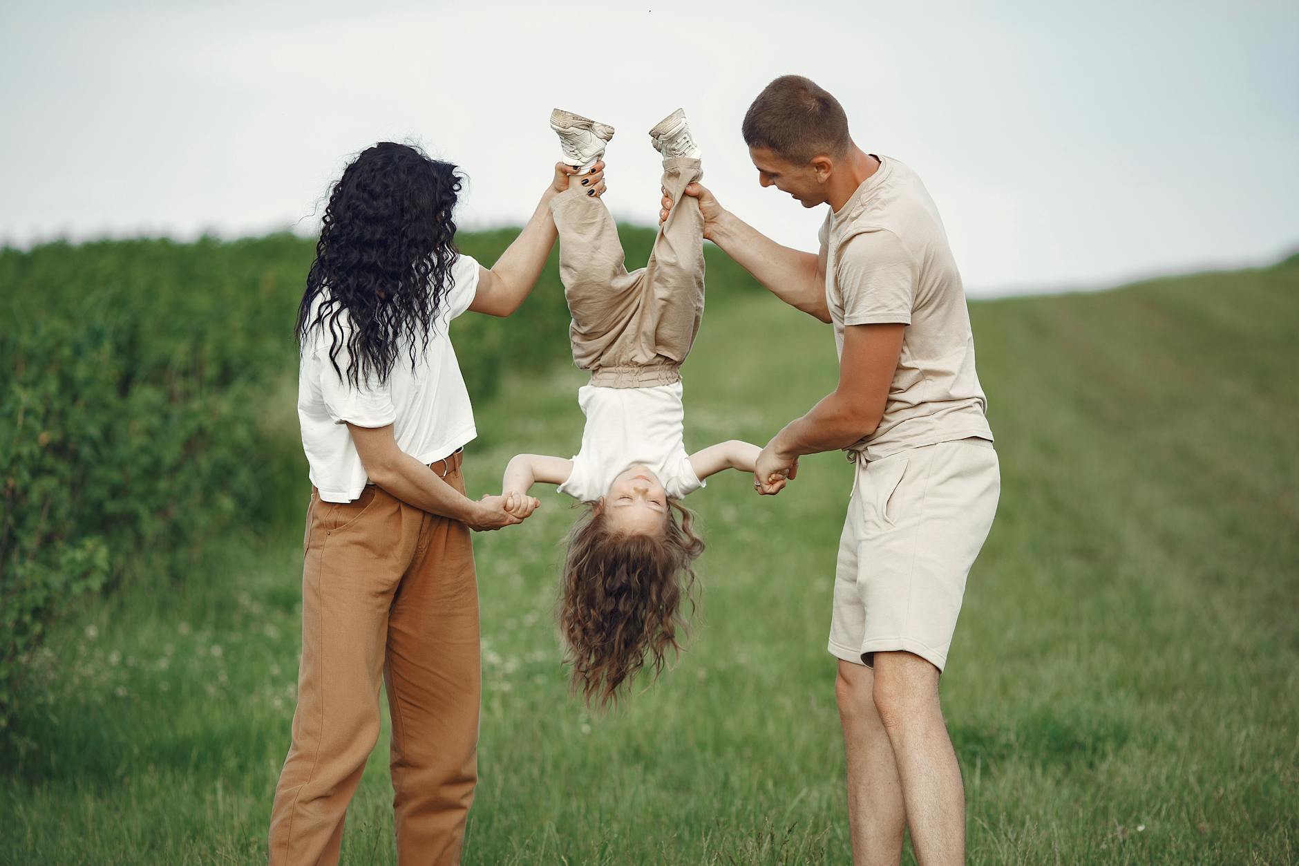 A joyful family enjoys outdoor play, lifting their child upside down in a green field. - co-parenting spring break