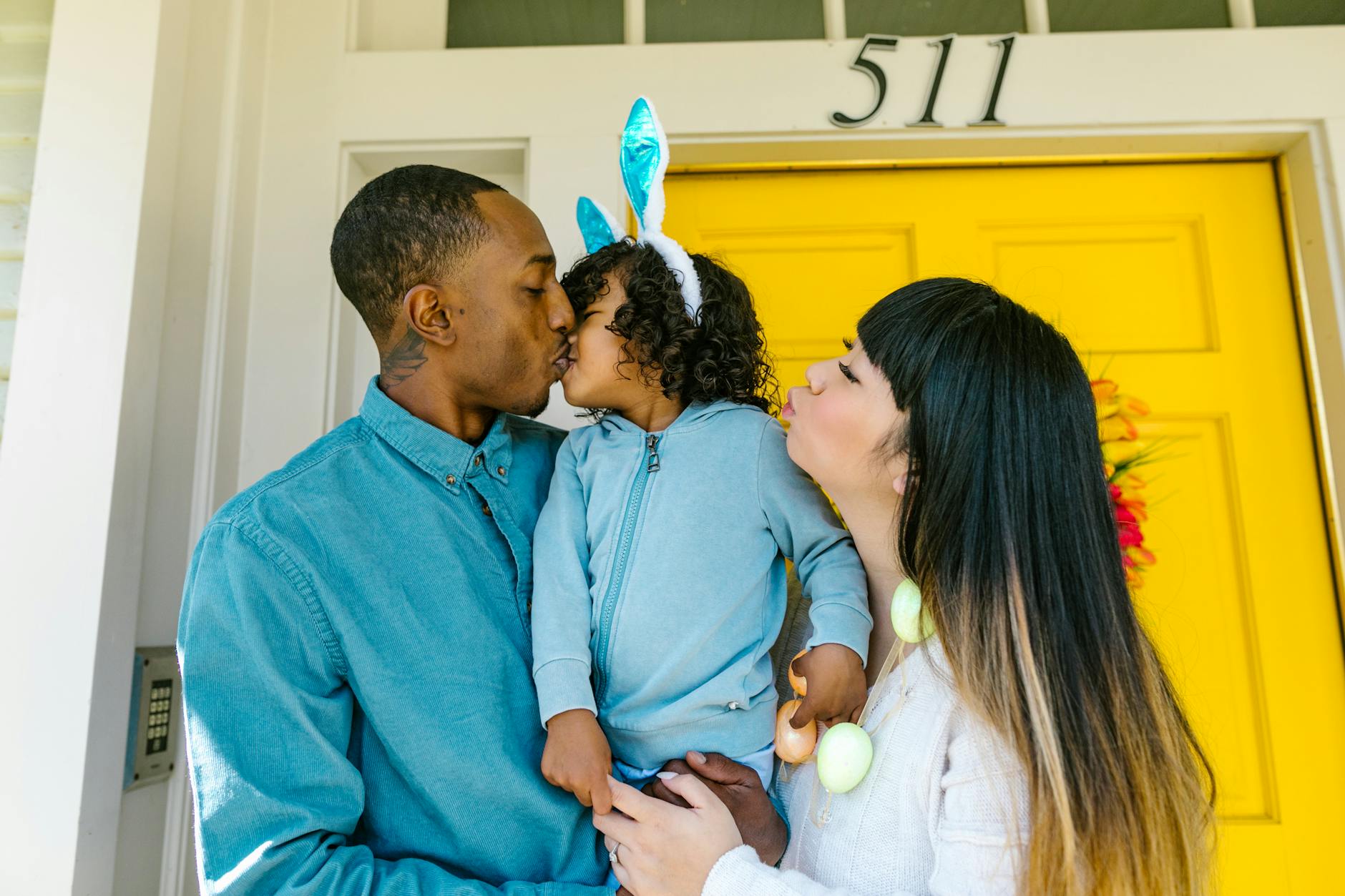 Interracial family enjoying Easter, exchanging kisses with a child wearing bunny ears. - co-parenting spring break