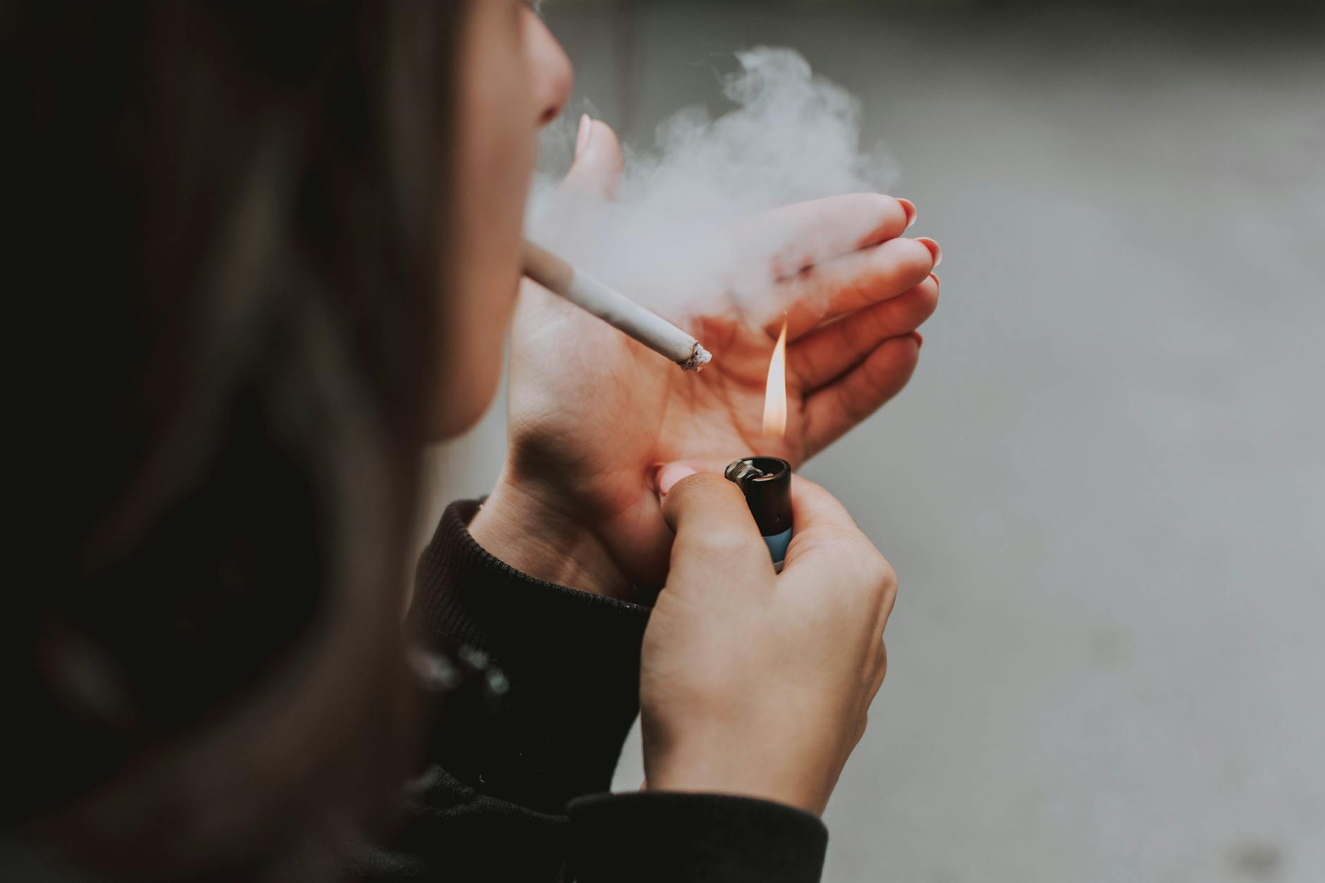 Close-up of a woman lighting a cigarette outdoors with a lighter, smoke visible. - communication habits