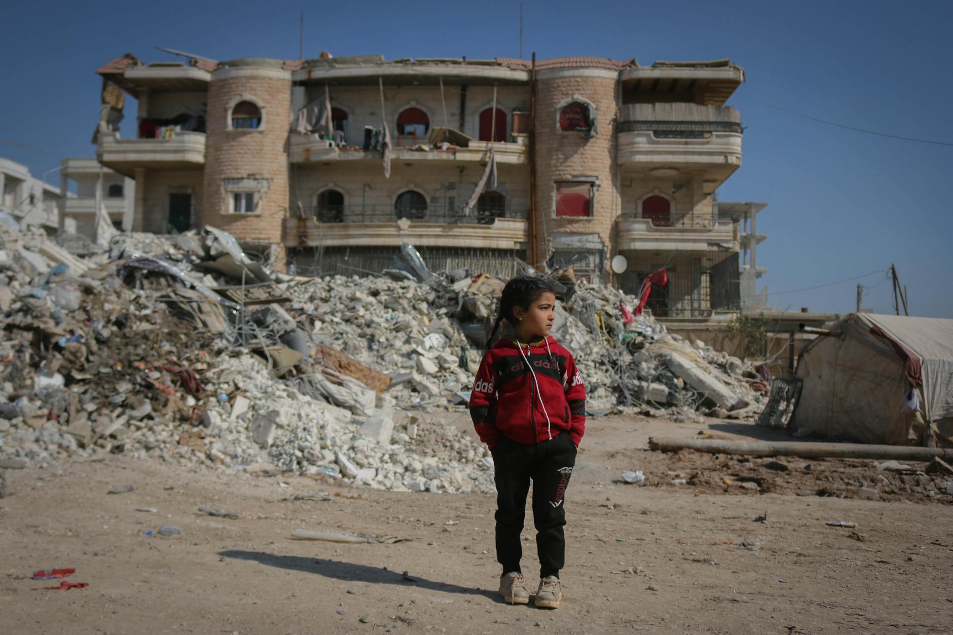 A girl stands in front of a destroyed building in Idlib, Syria, highlighting the impact of conflict. - what is conflict