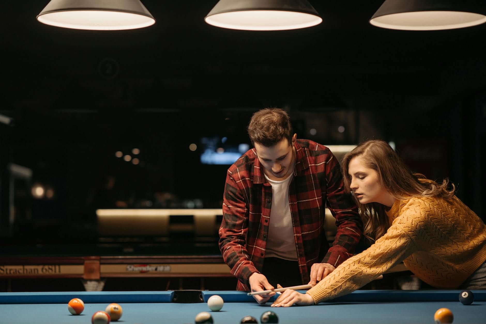 A young couple enjoys learning billiards together in a warmly lit room, sharing a recreational moment. - couple communication skills