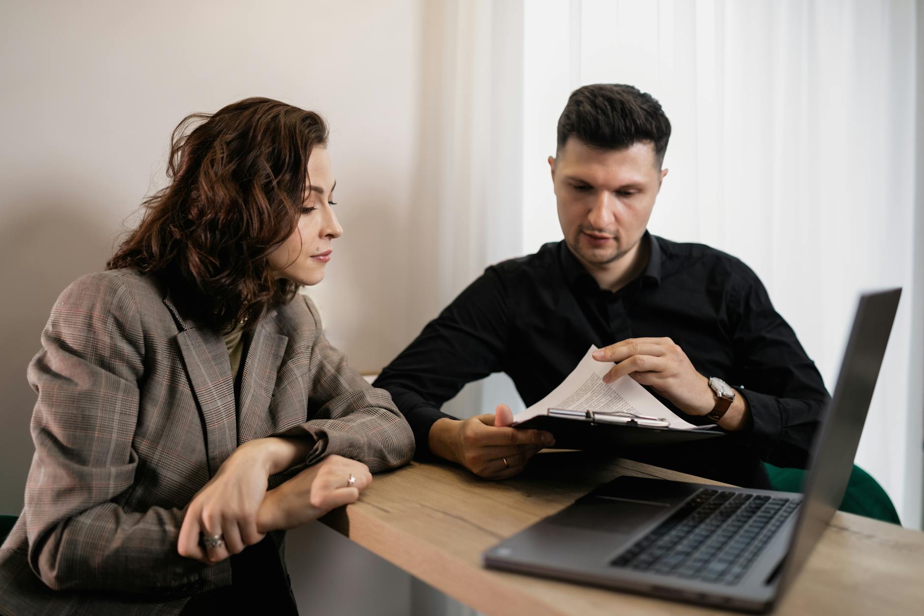 Two professionals discussing documents at a desk with a laptop, focused on collaboration. - couple communication skills