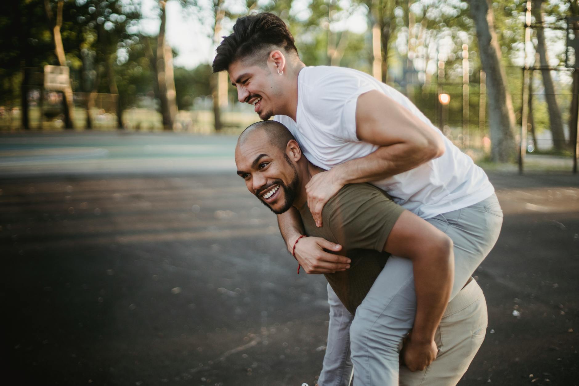 Joyful gay couple having fun with a piggyback ride in a park, showcasing love and happiness. - couple energy boundaries
