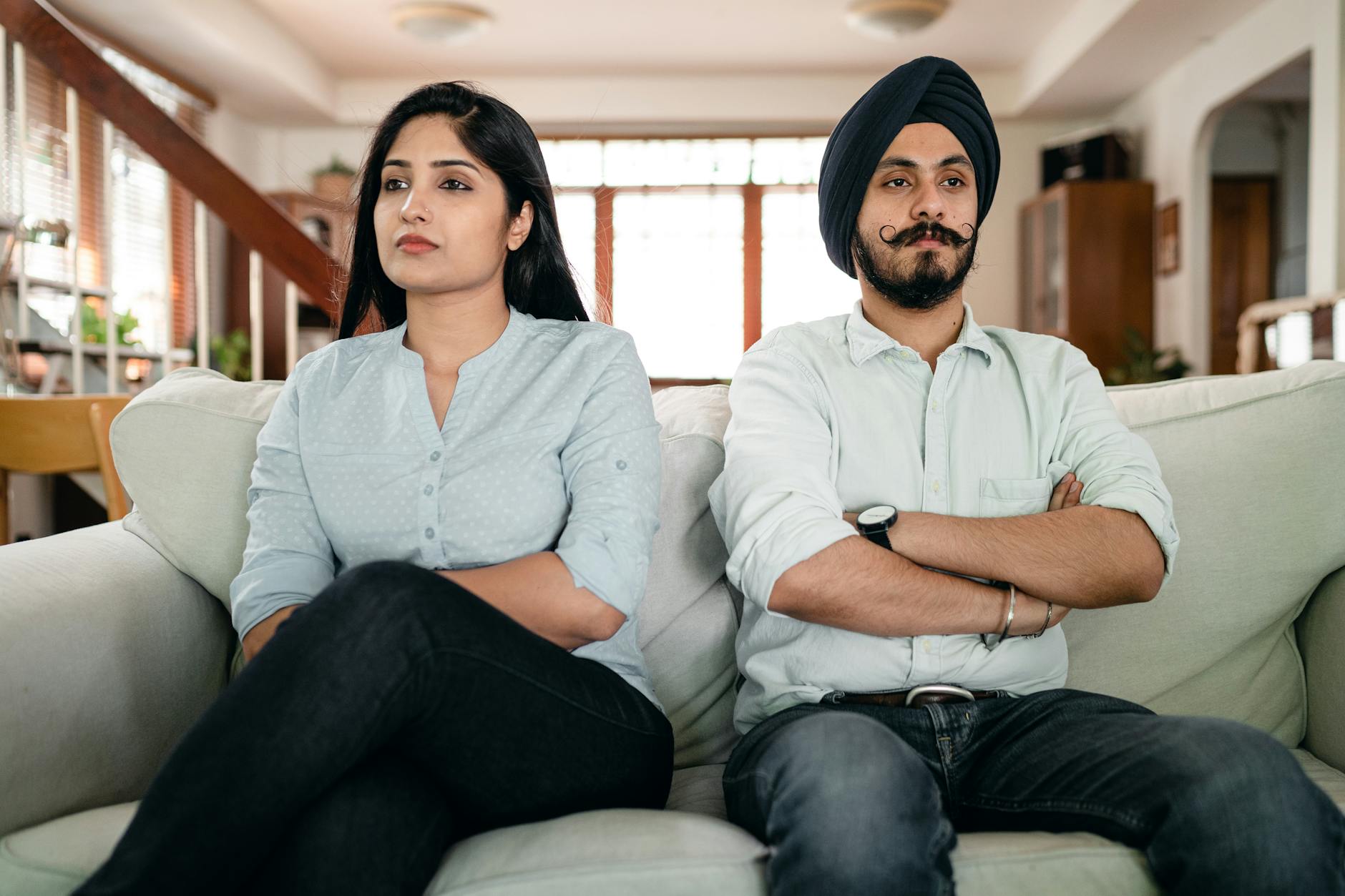 Resentful young Indian couple ignoring each other while sitting on couch together with crossed arms - couple resentment spring