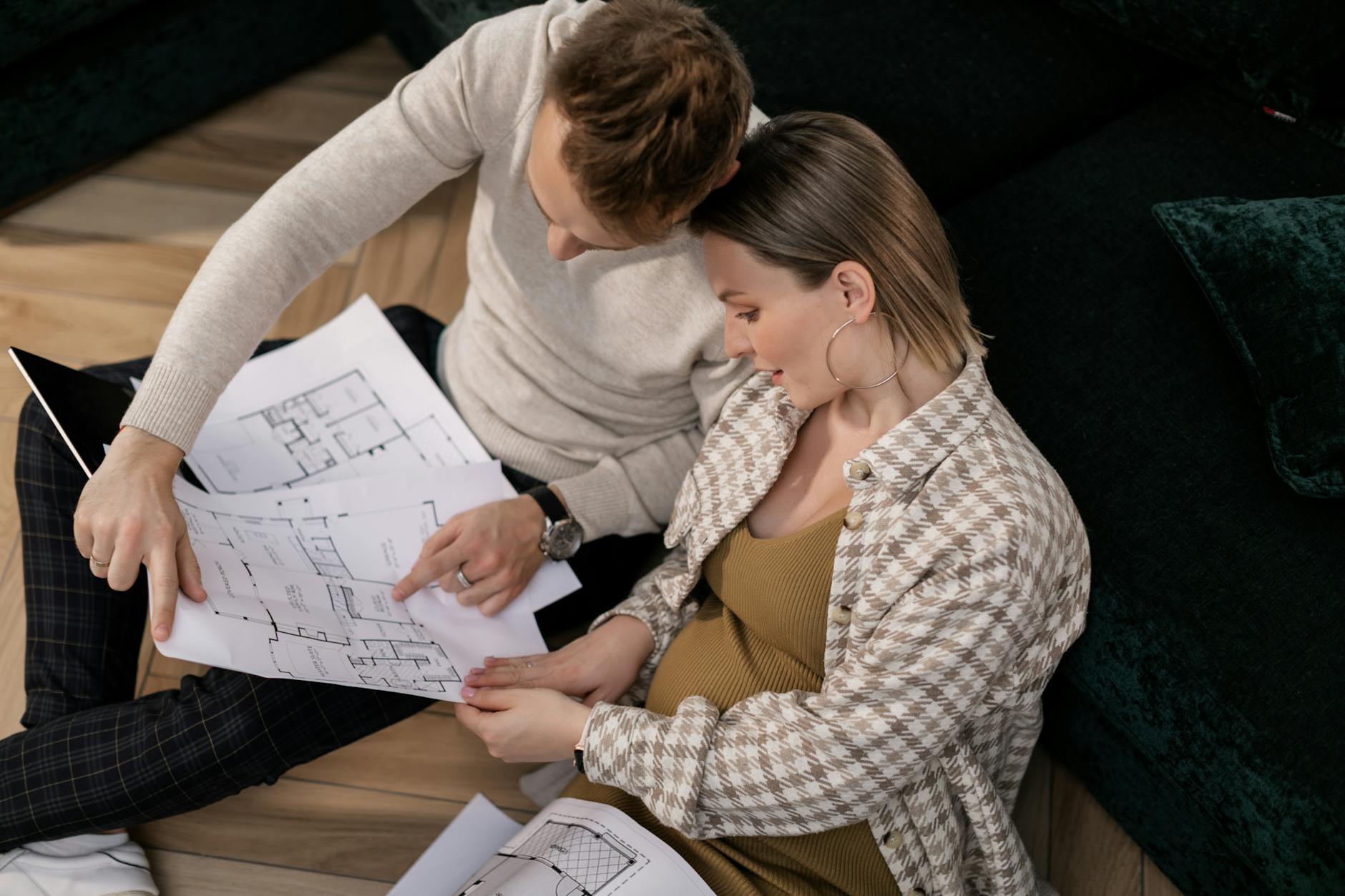 A couple sits on the floor reviewing house blueprints in their living room. - couple travel planning communication