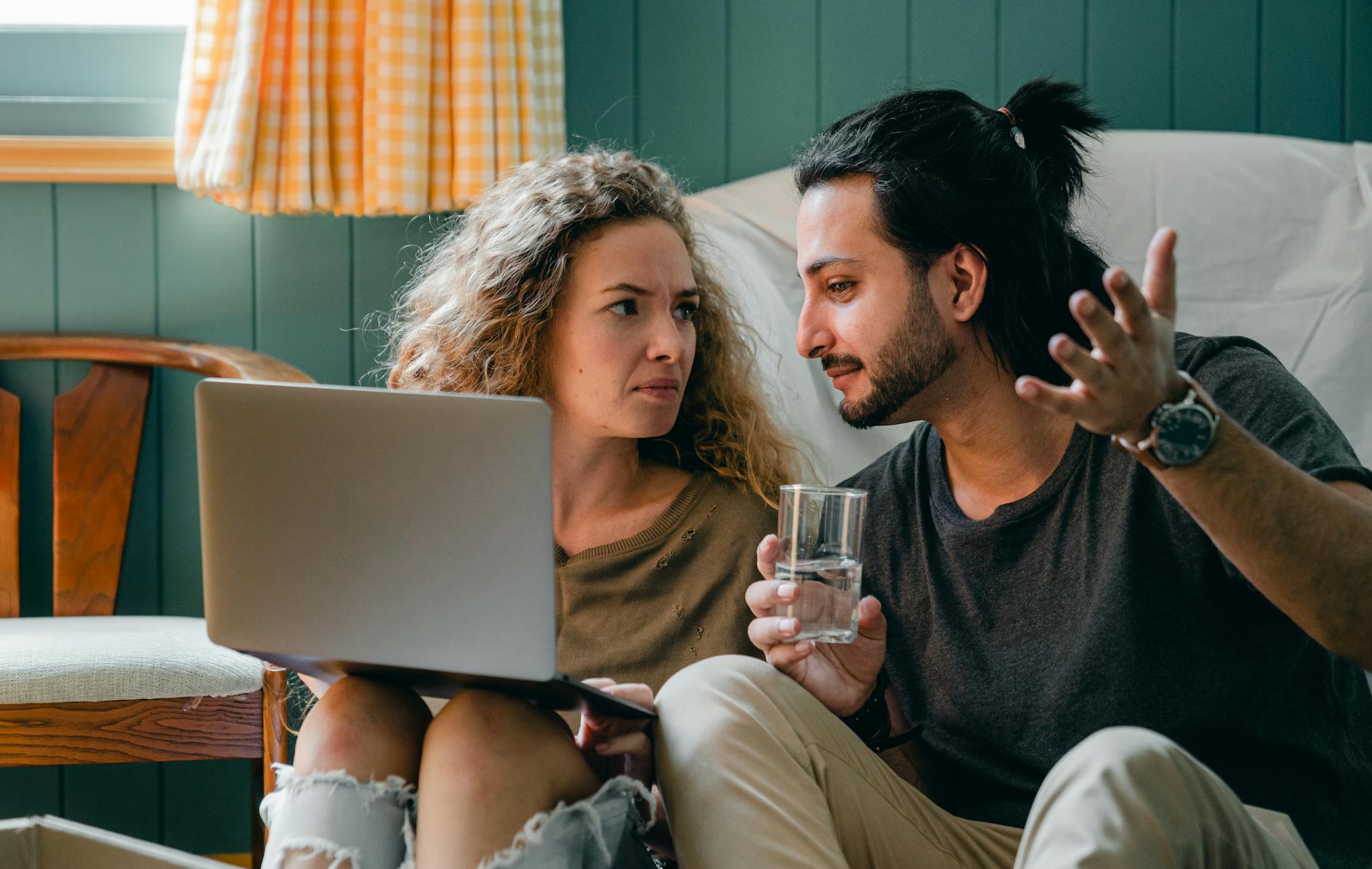 A couple sits on the floor, engaged in conversation, using a laptop in a cozy apartment. - couples communication needs