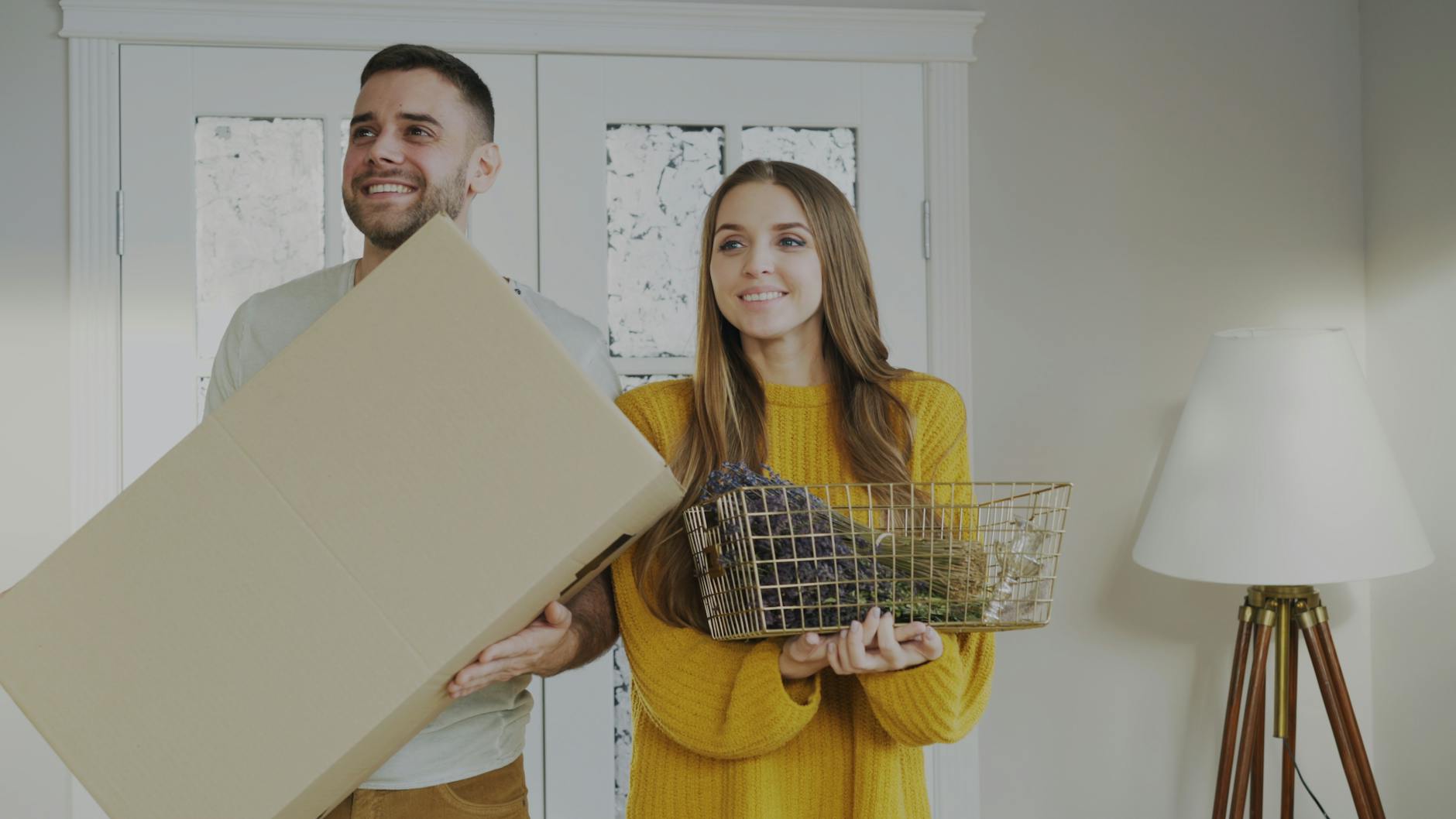 A happy couple carrying a box and decor items as they move into a new home. - couples therapy new beginnings
