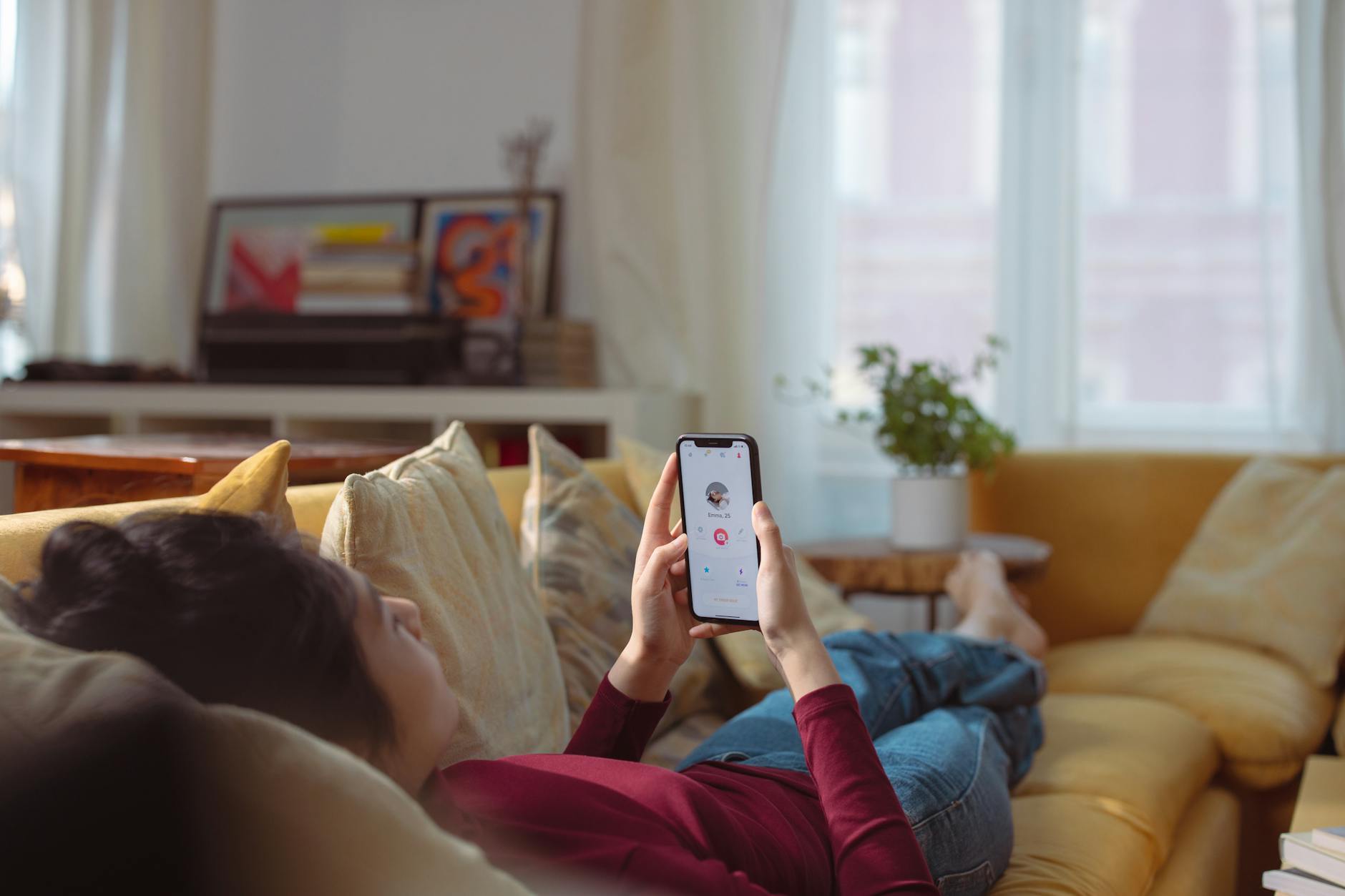 Woman relaxing and using a dating app on her smartphone while lying on a sofa indoors. - dating app refresh