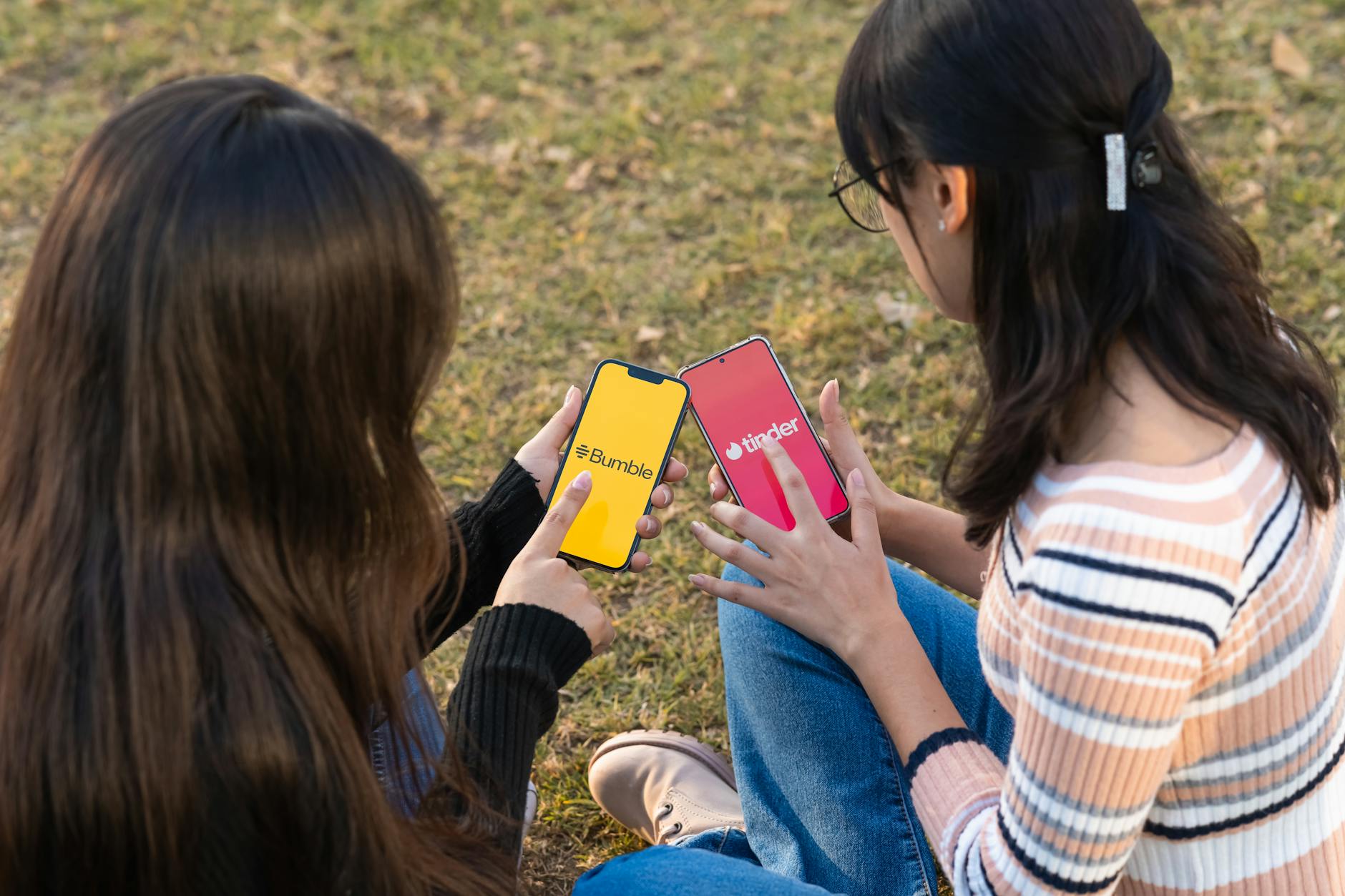 Two women using dating apps Bumble and Tinder on smartphones in a park setting. - dating app refresh
