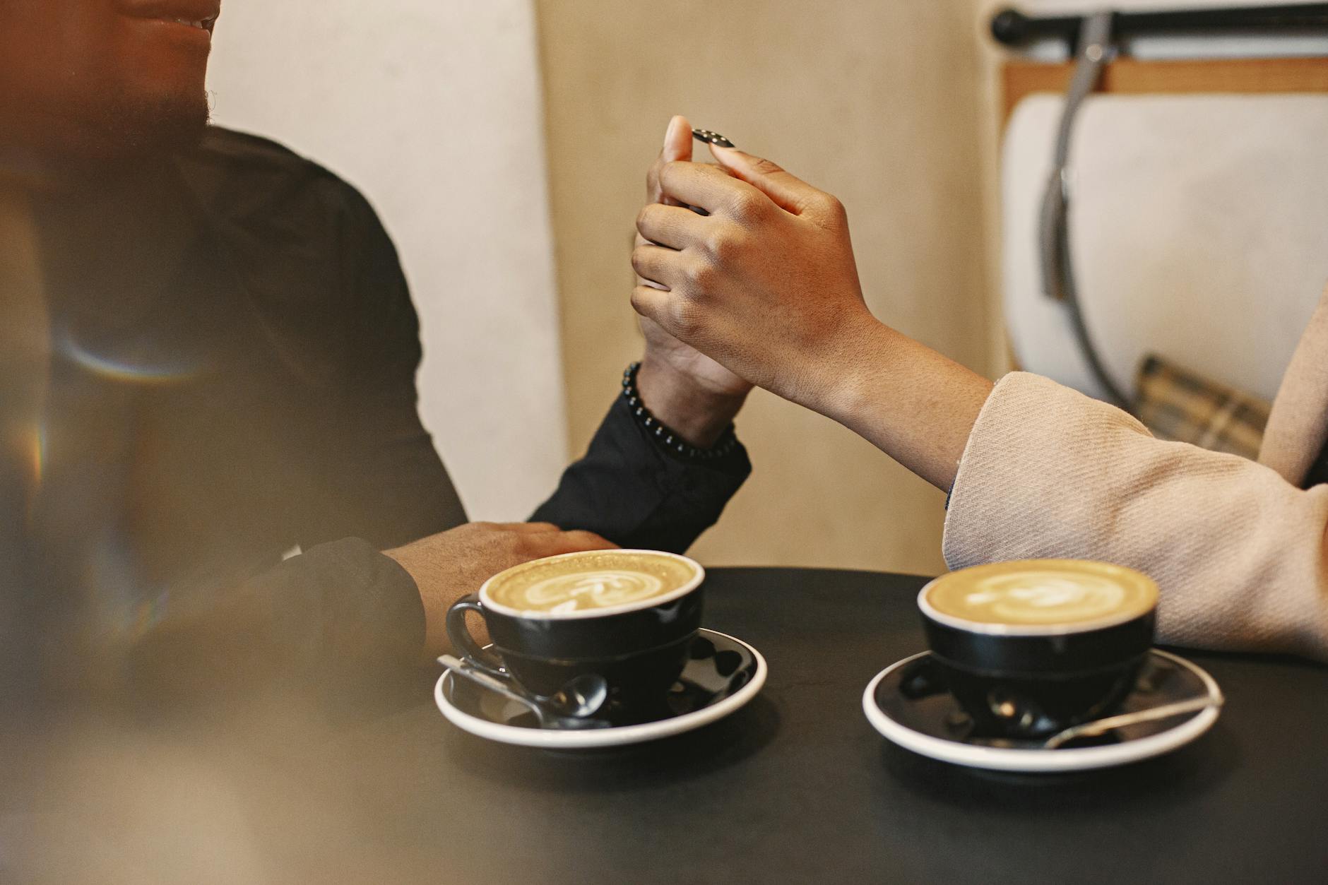 A couple holding hands over coffee in a cozy cafe setting. - dating tips introverts