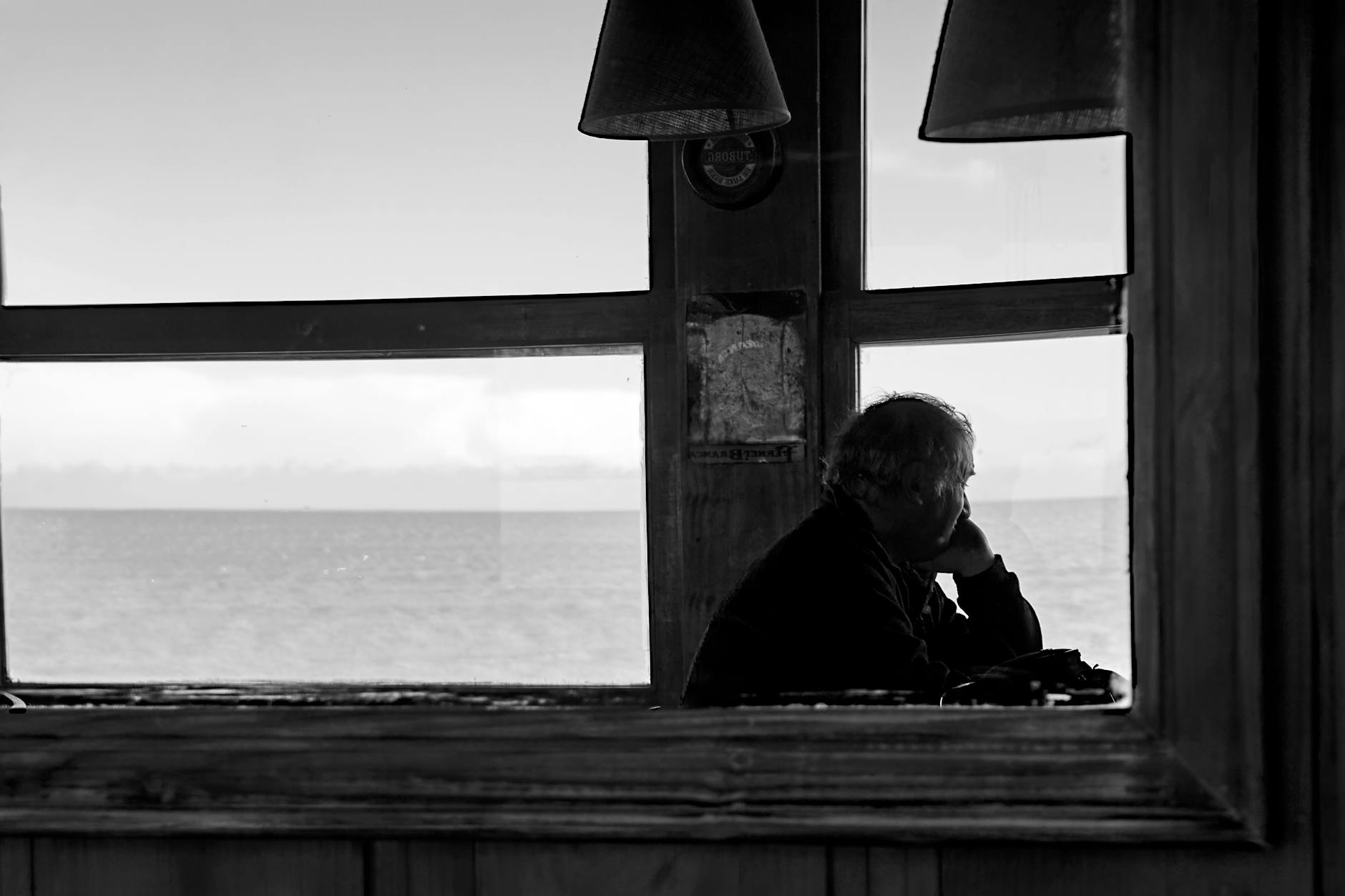 Silhouette of a man looking out a window at the sea in a monochrome view, reflecting solitude. - declutter negative thoughts