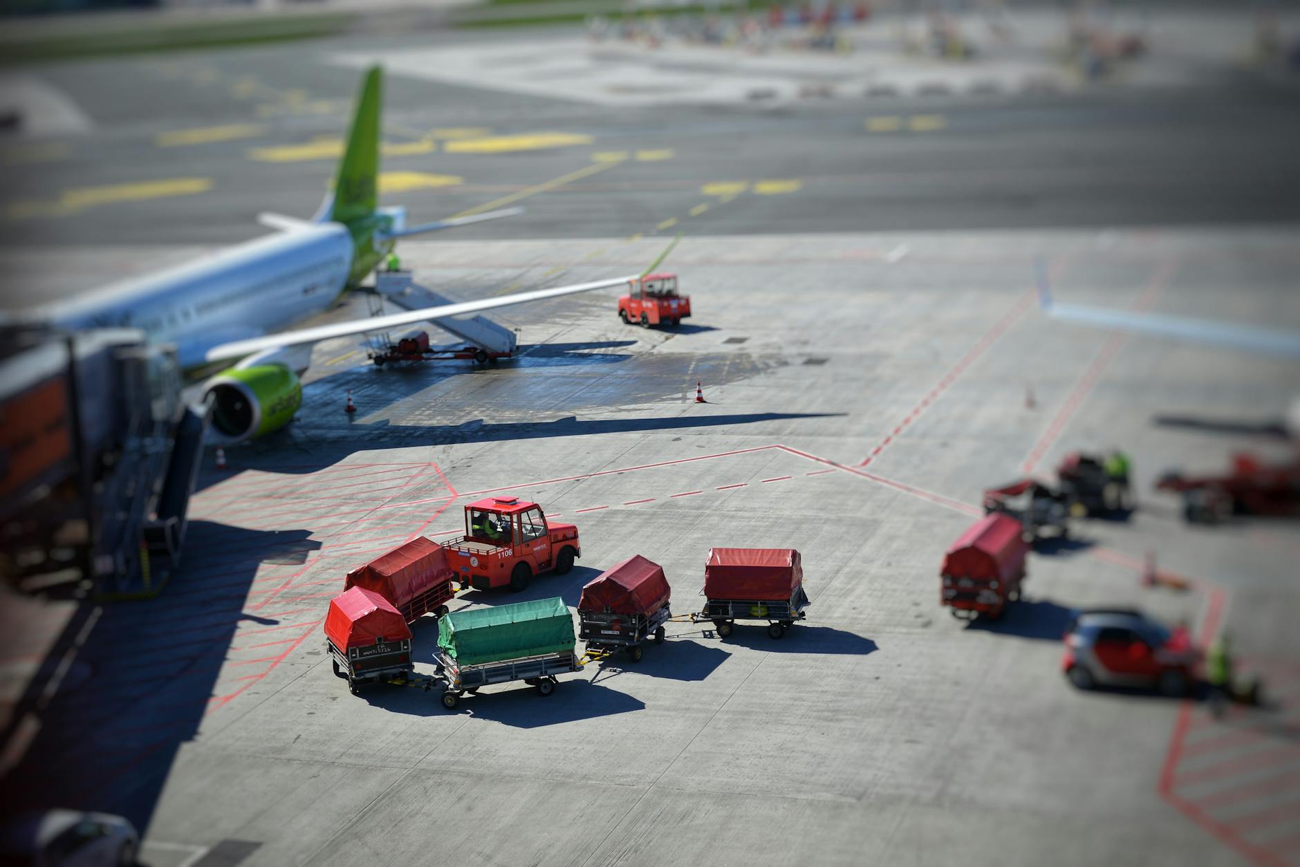 Sunlit airplane and baggage carts on airport tarmac, captured from above, showcasing transportation dynamics. - declutter relationship baggage