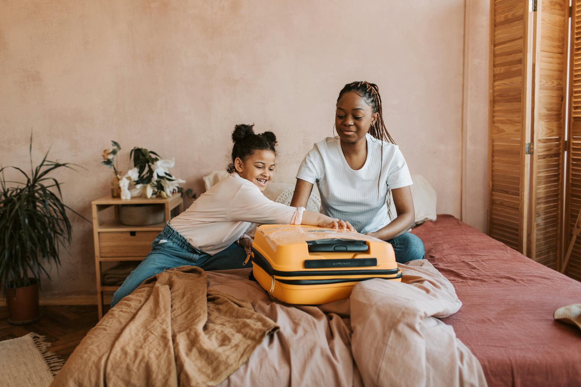A mother and daughter share a joyful moment packing a suitcase on the bed. - declutter relationship baggage