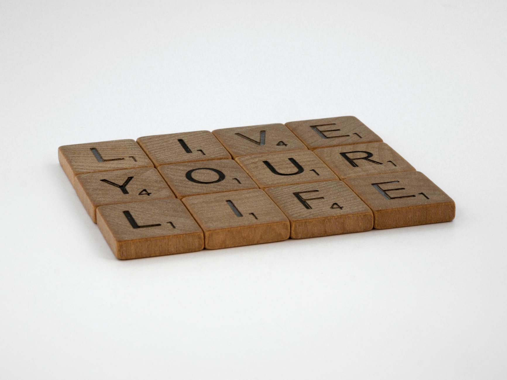 Wooden Scrabble tiles spell out 'Live Your Life' on a white surface. Encouraging and minimalist. - declutter your mind