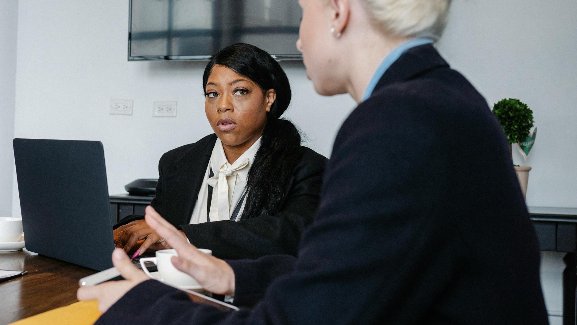 Serious diverse coworkers in formal wear gathering at table with gadgets and discussing business strategy while working in office - define assertive communication