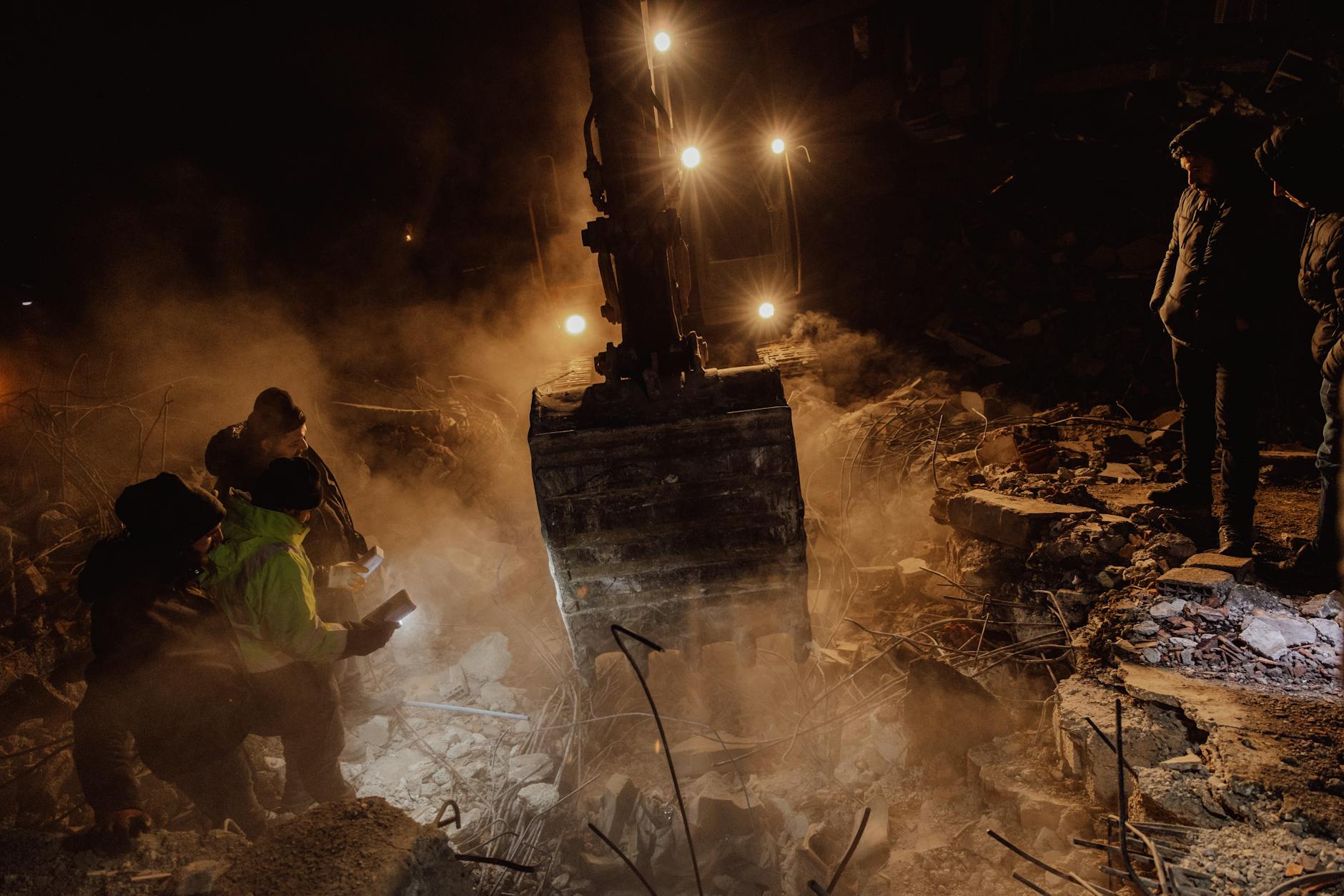 Emergency workers conduct a night rescue in debris after a disaster, illuminated by harsh lights. - difficult conversations