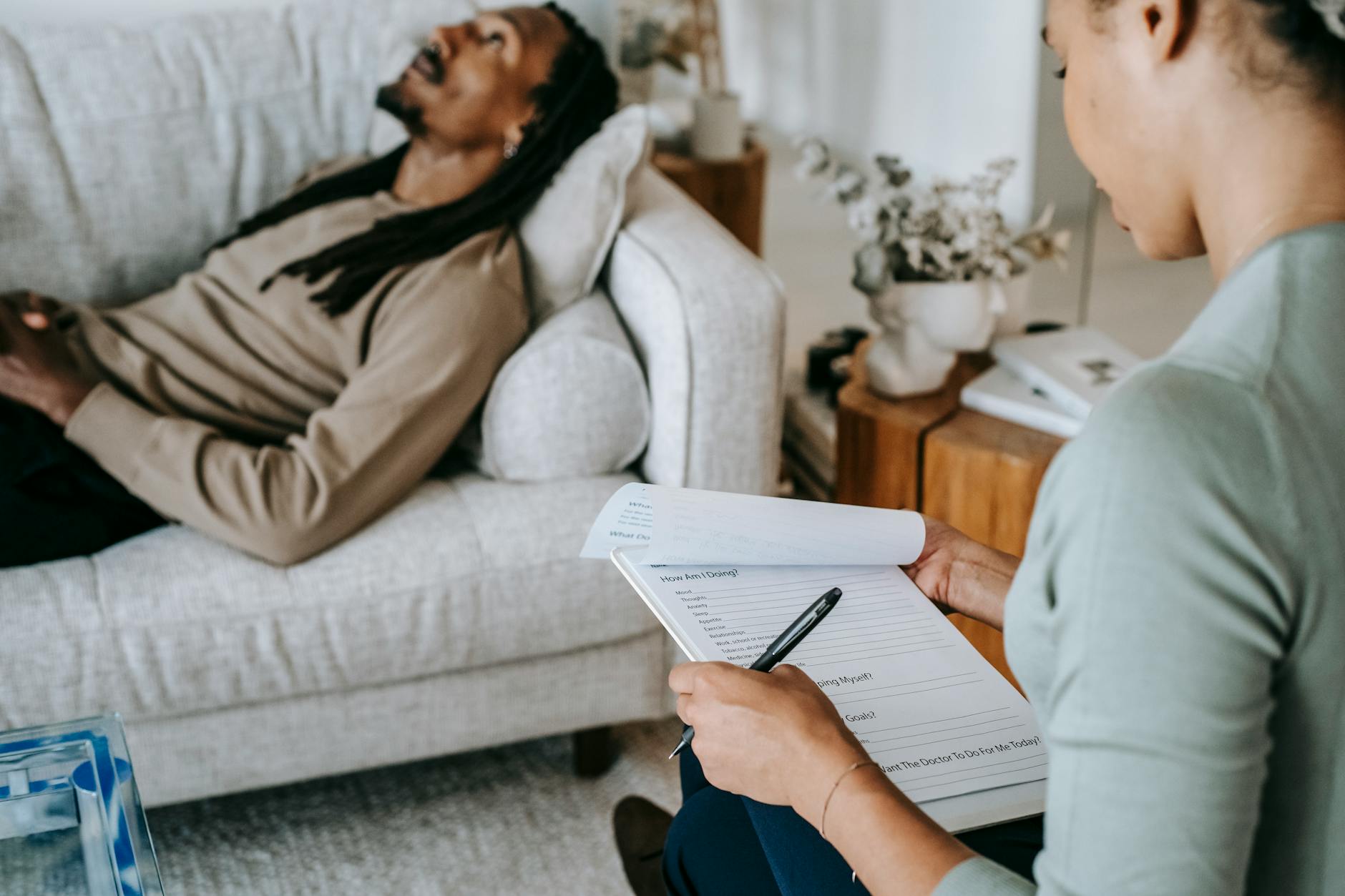 A therapist with clipboard assists a man during a home therapy session on a sofa. - dream analysis therapy