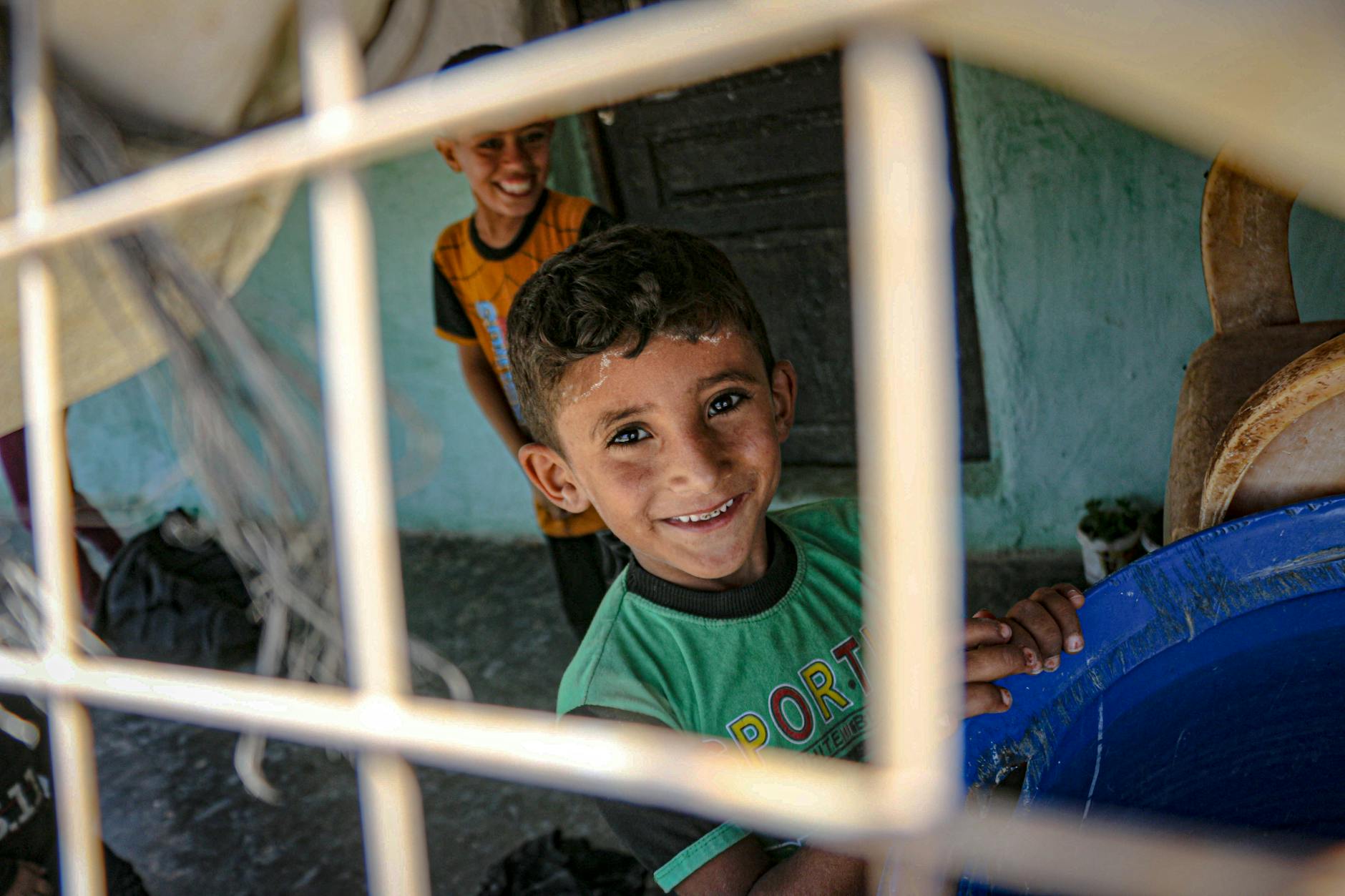 A young boy smiles warmly behind a bar in Idlib, Syria, showcasing resilience and joy. - emotional resilience children
