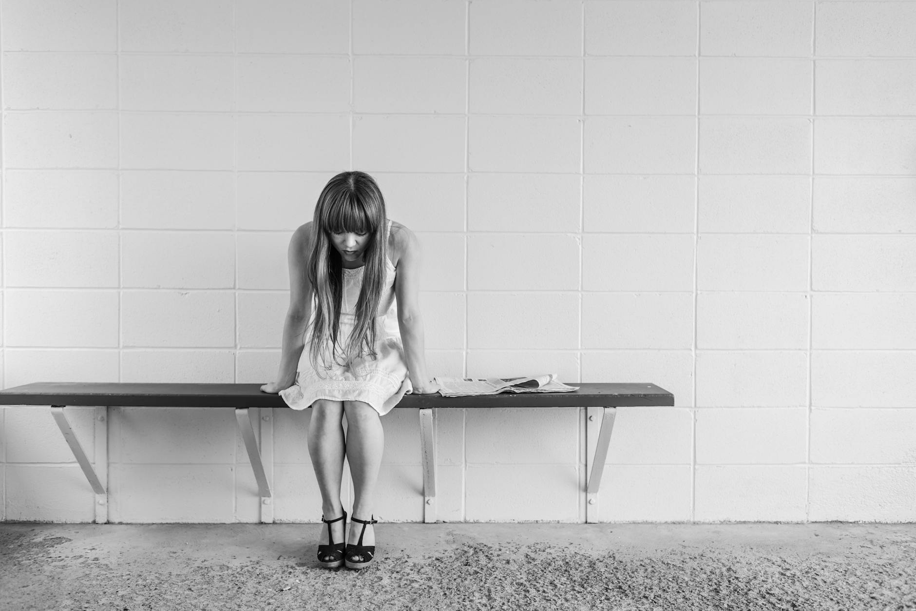 A black and white photo of a woman in thought, sitting on a bench indoors, portraying solitude. - empty nest depression