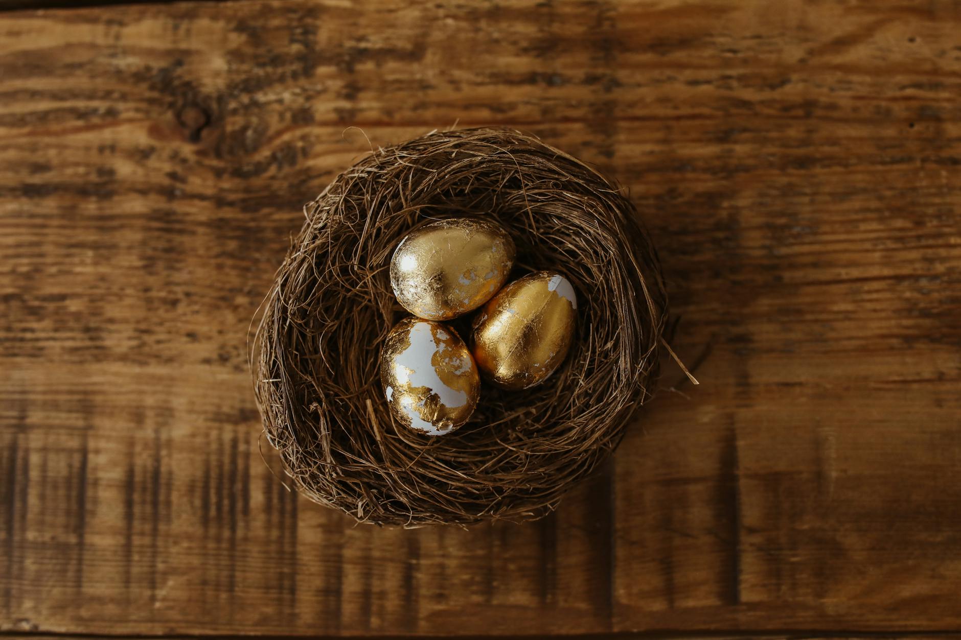 Close-up of golden eggs in a nest on a wooden table, symbolizing wealth and prosperity. - empty nest syndrome