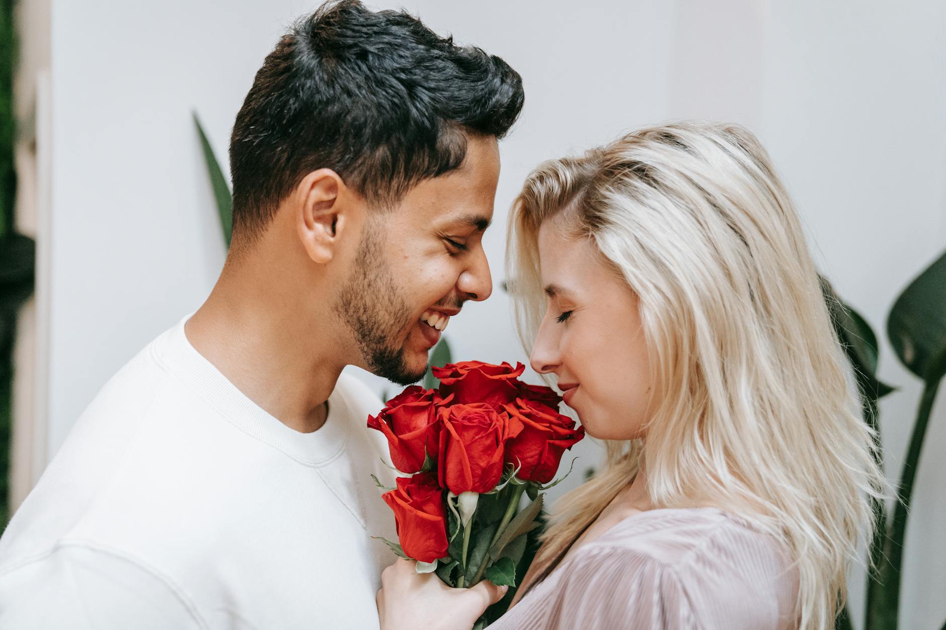 A loving interracial couple shares a tender moment with a bouquet of red roses indoors. - express gratitude partner