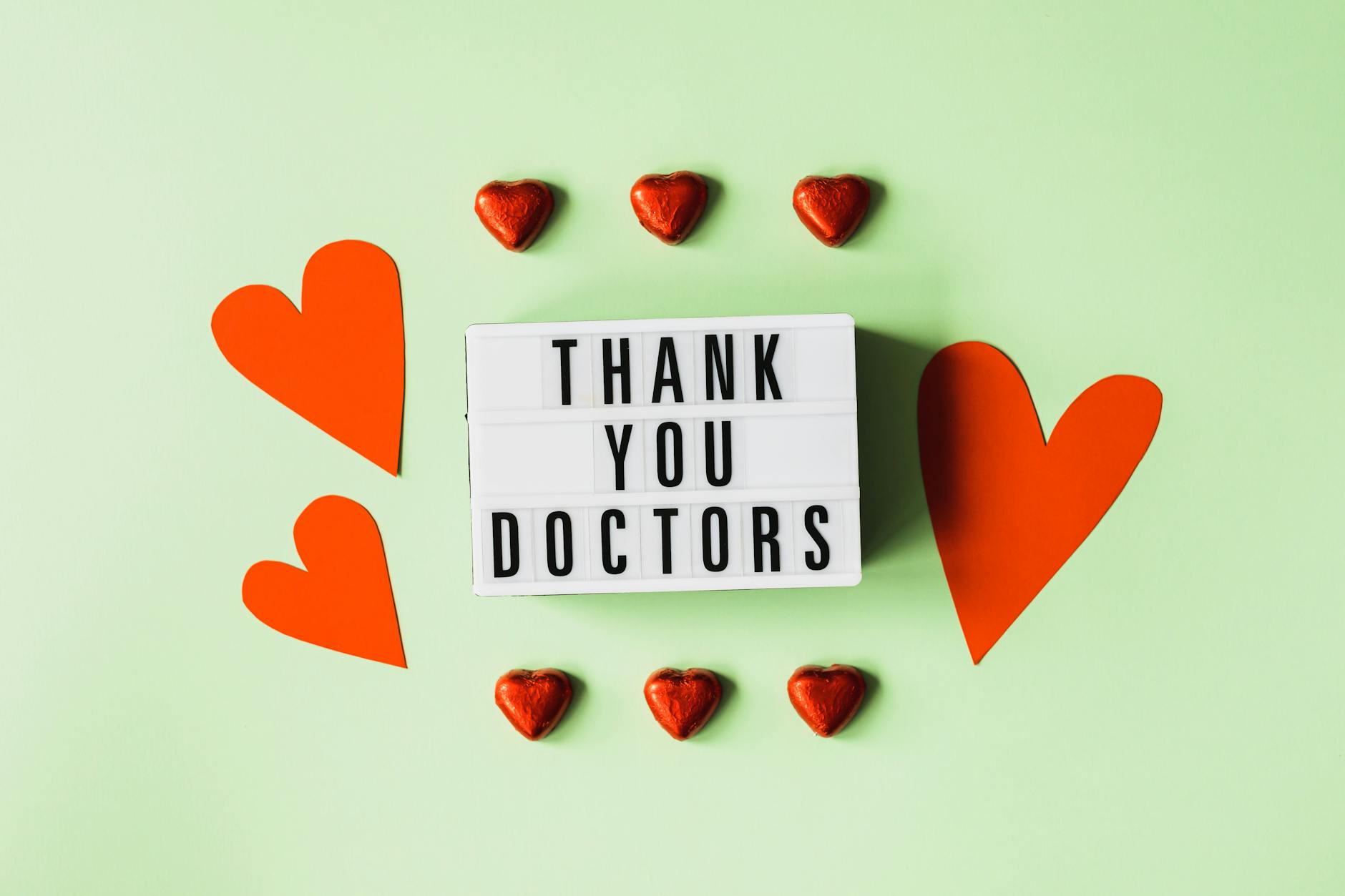 Top view of red heart shaped decorative elements and white retro light box with THANK YOU DOCTORS gratitude message arranged on green background - express gratitude relationships