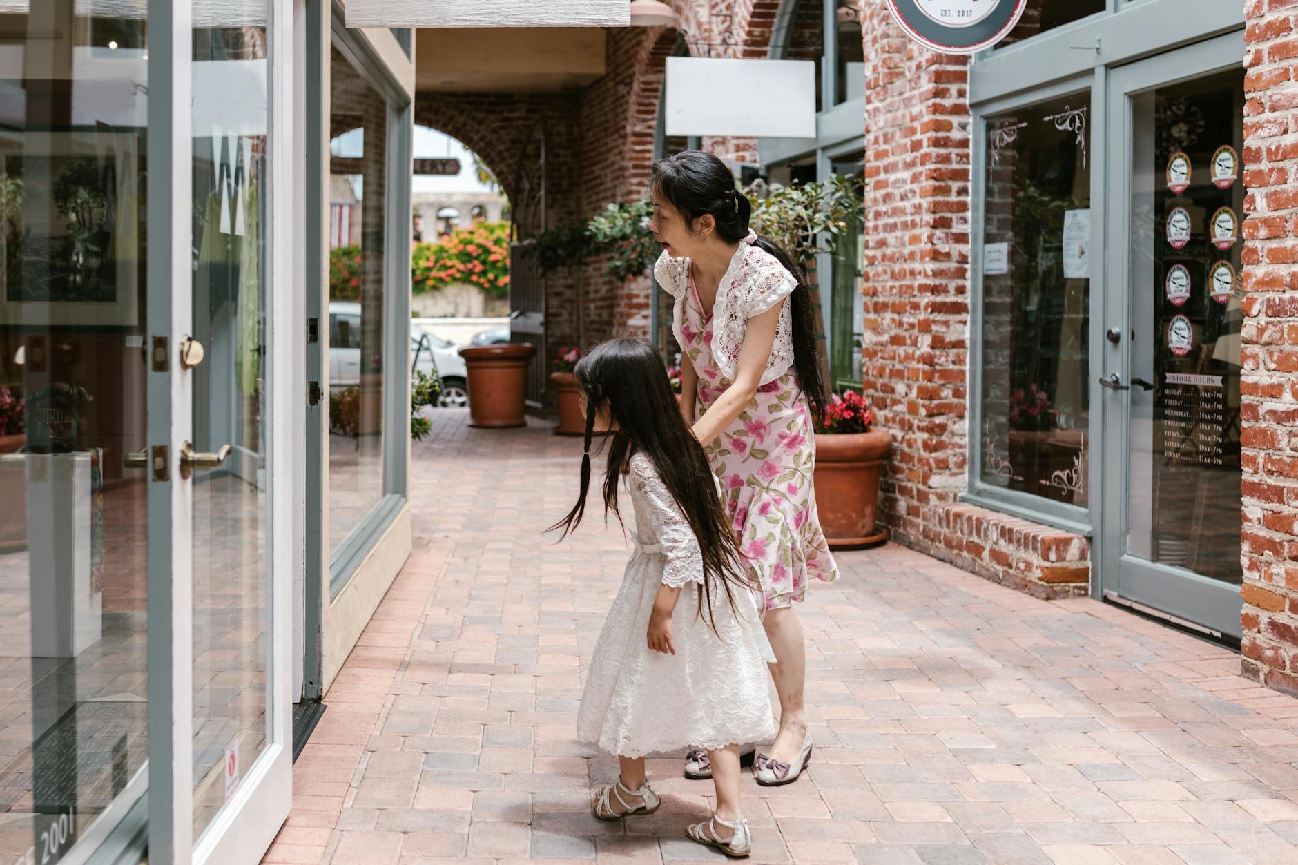 A mother and daughter window shopping in a charming urban brick-lined walkway. - express needs clearly