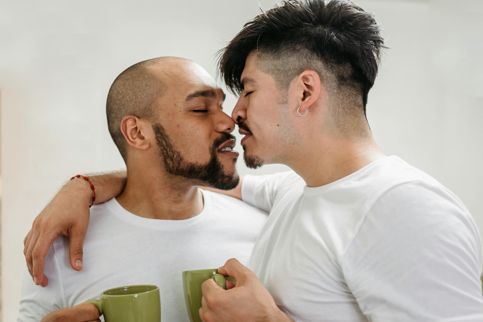 Two men sharing an intimate moment with coffee cups in a bright setting. - express needs couples