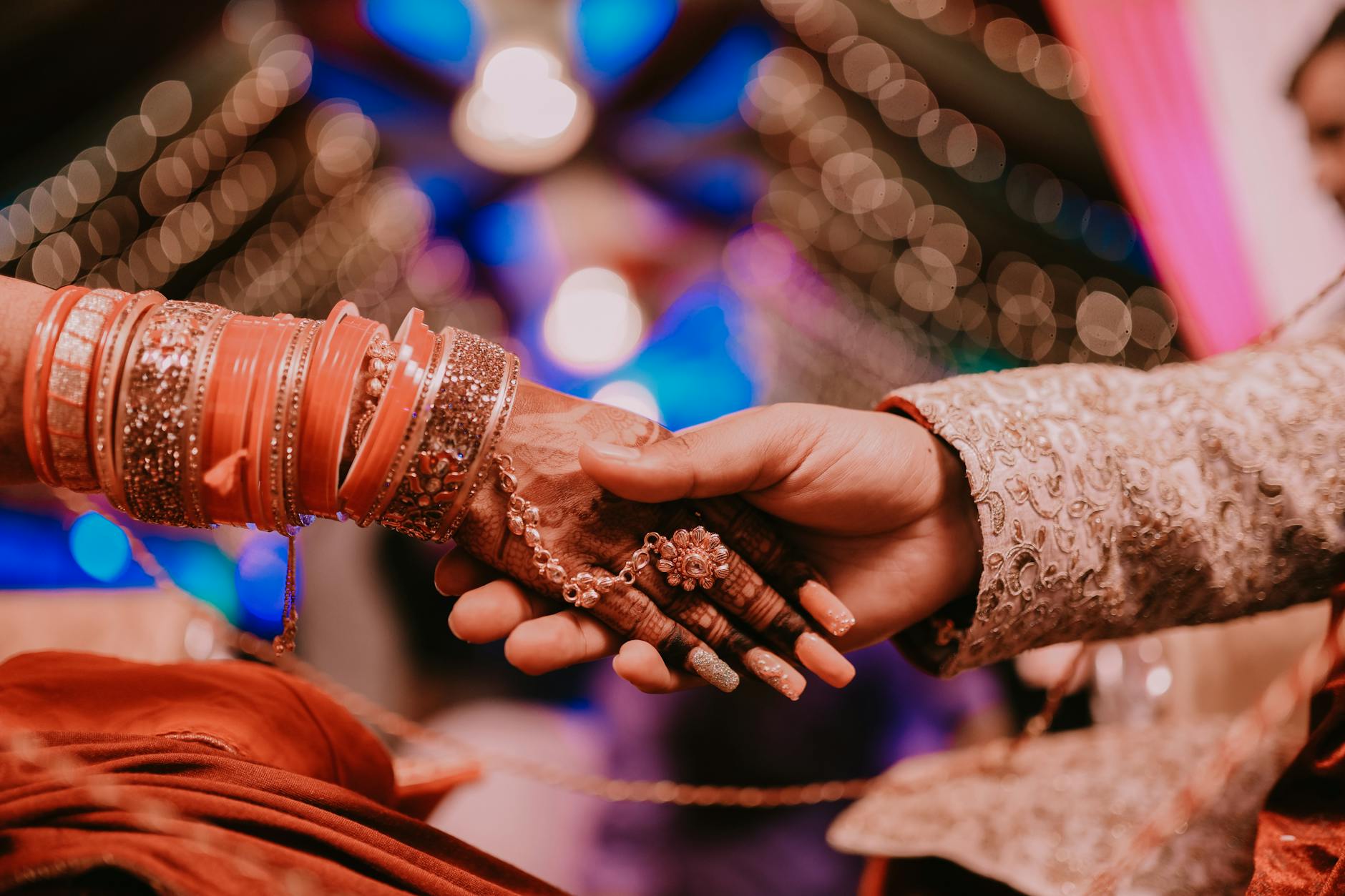 A close-up of a couple holding hands at an Indian wedding, adorned with henna and bangles, symbolizing love and unity. - express needs marriage