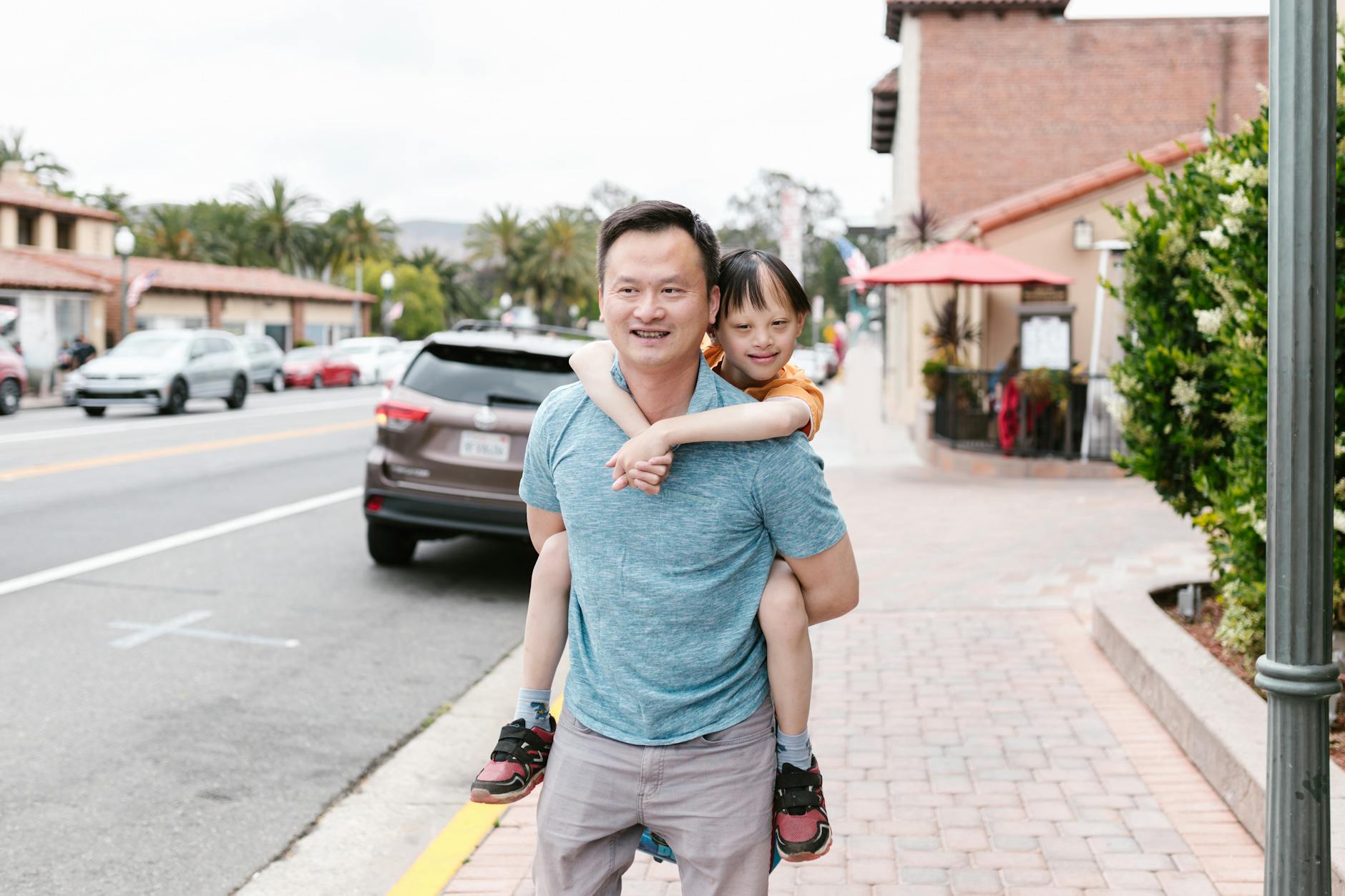 A joyful Asian father giving his child a piggyback ride on a city street. - express relationship needs