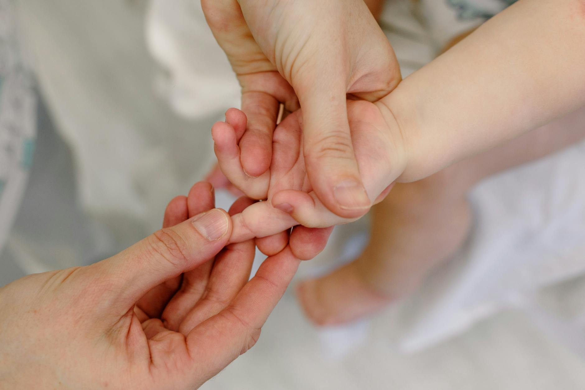 Close-up of an adult giving a gentle massage to a baby's hand, showcasing tender care and nurturing touch. - family dynamics therapy