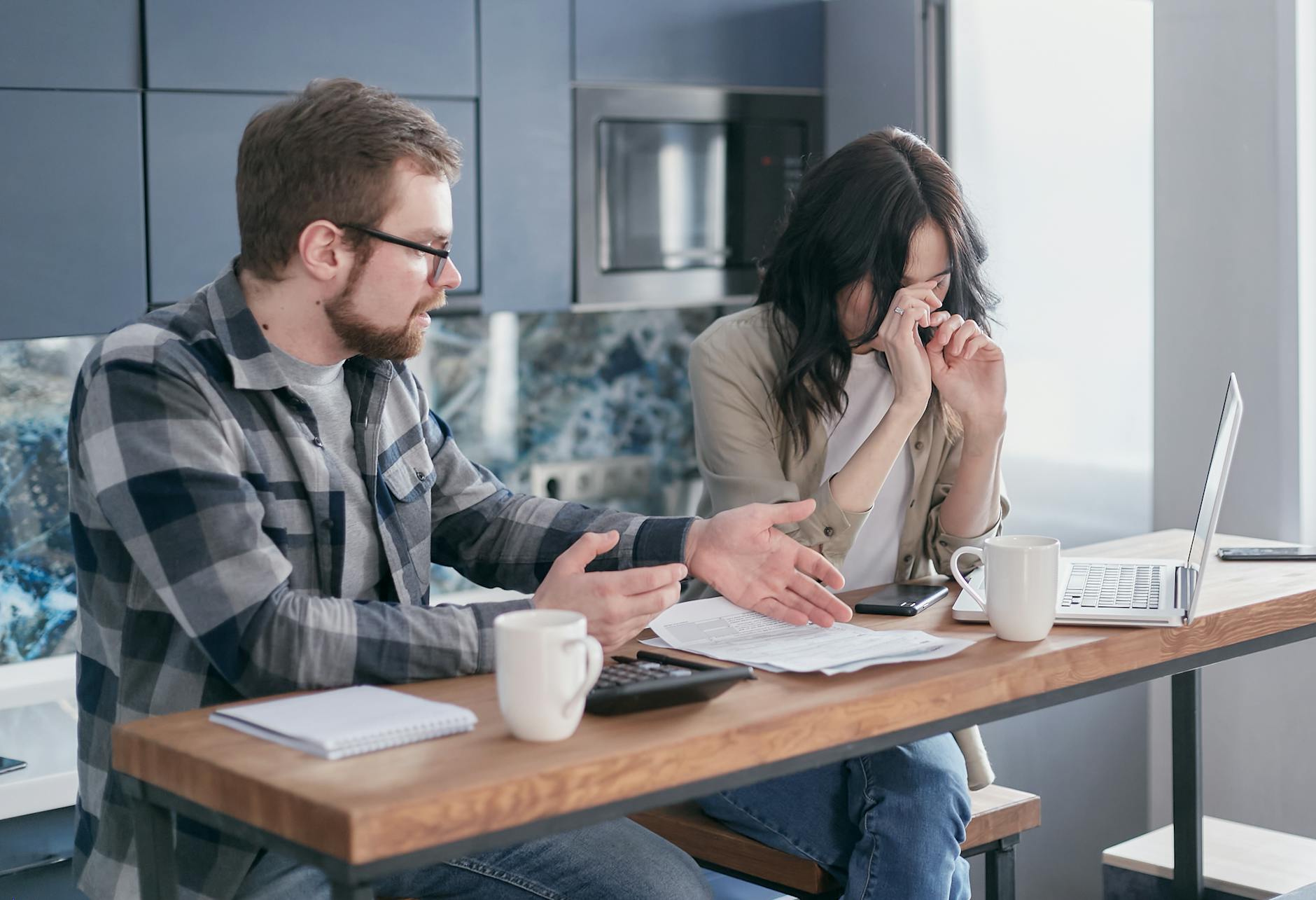 A couple sitting at a table indoors, visibly stressed while discussing bills and finances. - financial stress couple