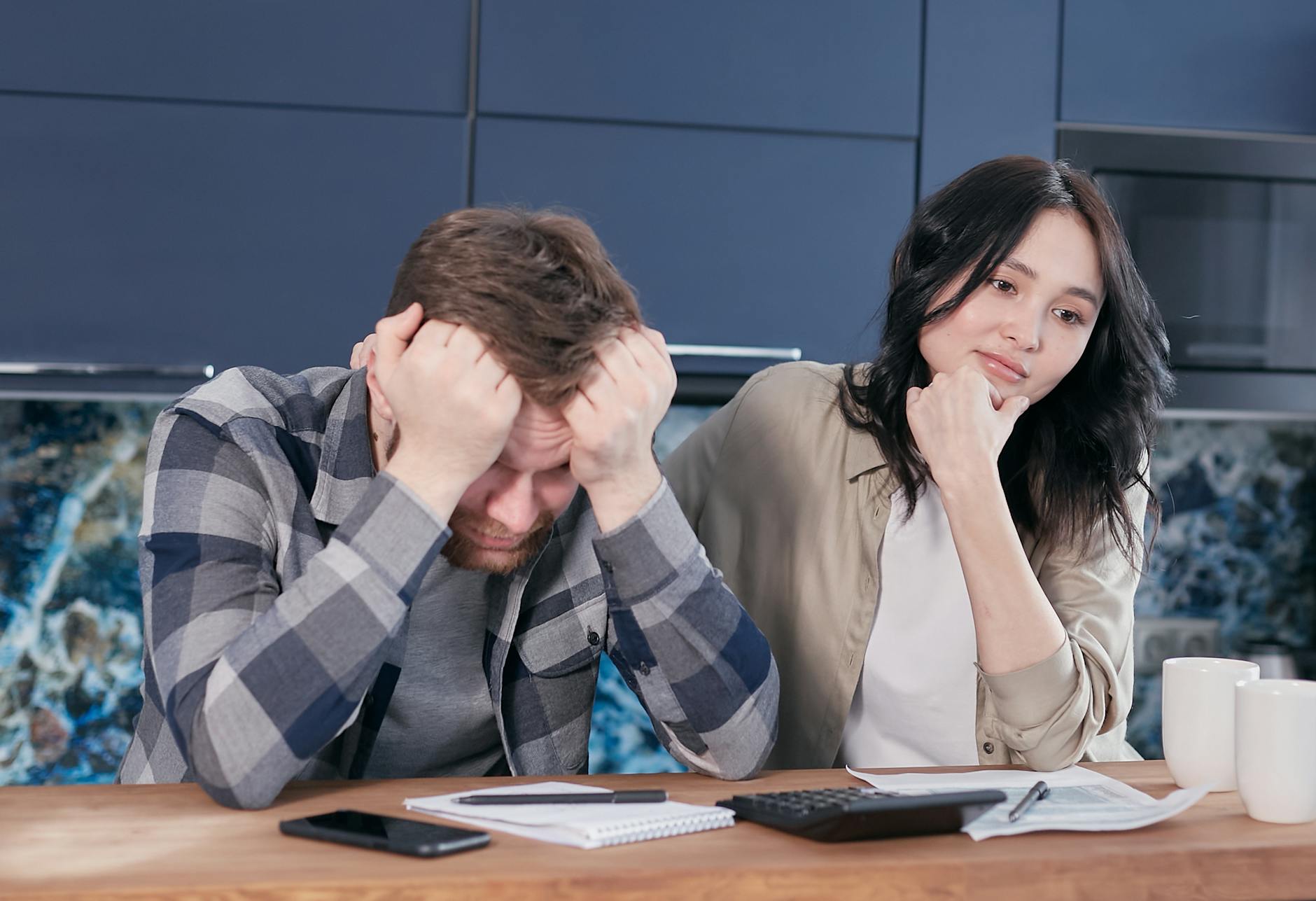 A couple looking worried while reviewing financial documents at a kitchen table. - financial stress couple