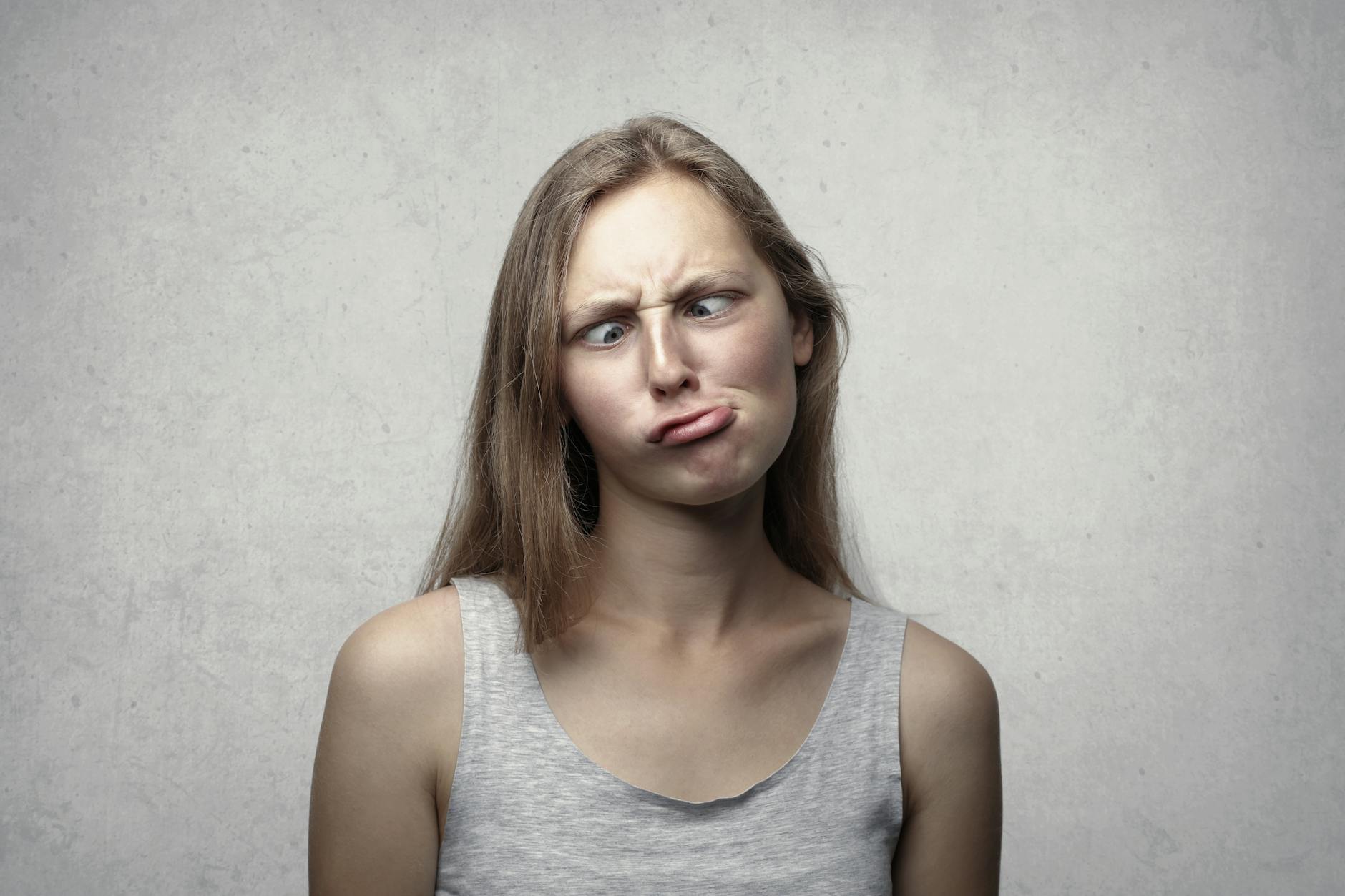 A woman with long hair making a silly expression, adding humor to an otherwise plain gray background. - funny marriage tips