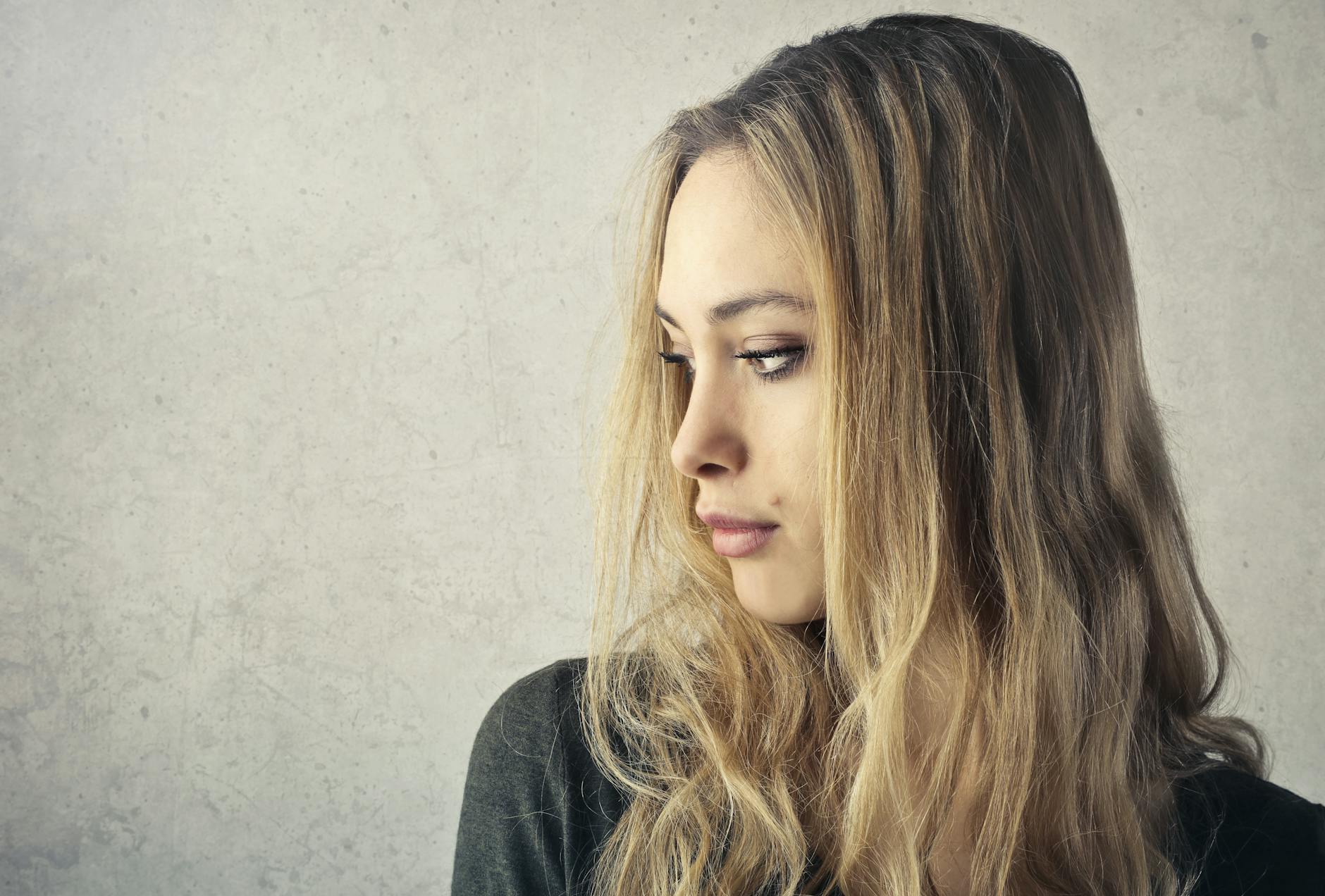 A pensive young woman with long blonde hair looking to the side against a neutral background. - gaslighting examples