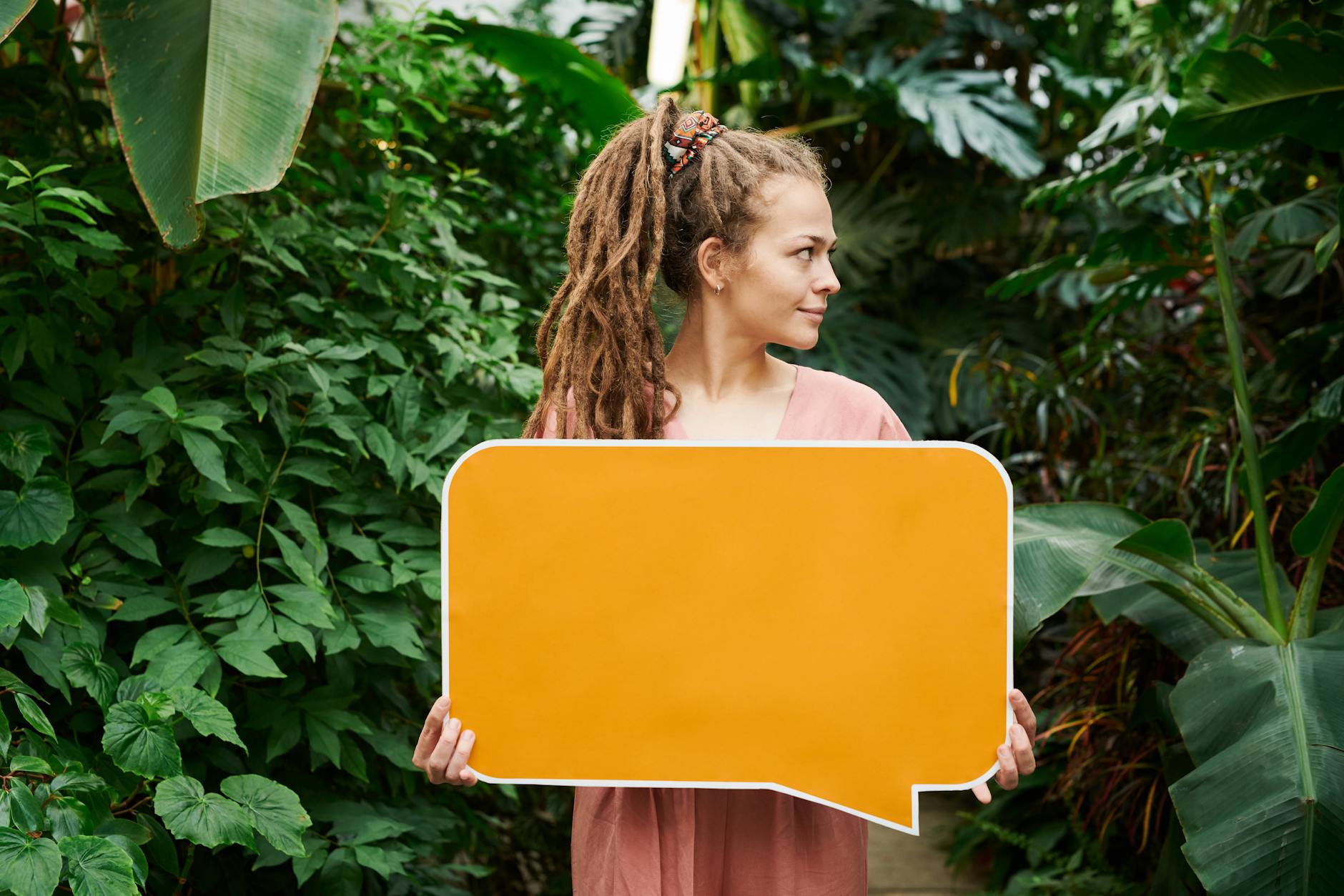 A woman with dreadlocks holds a blank orange sign in a vibrant green garden, providing perfect copy space. - gaslighting signs