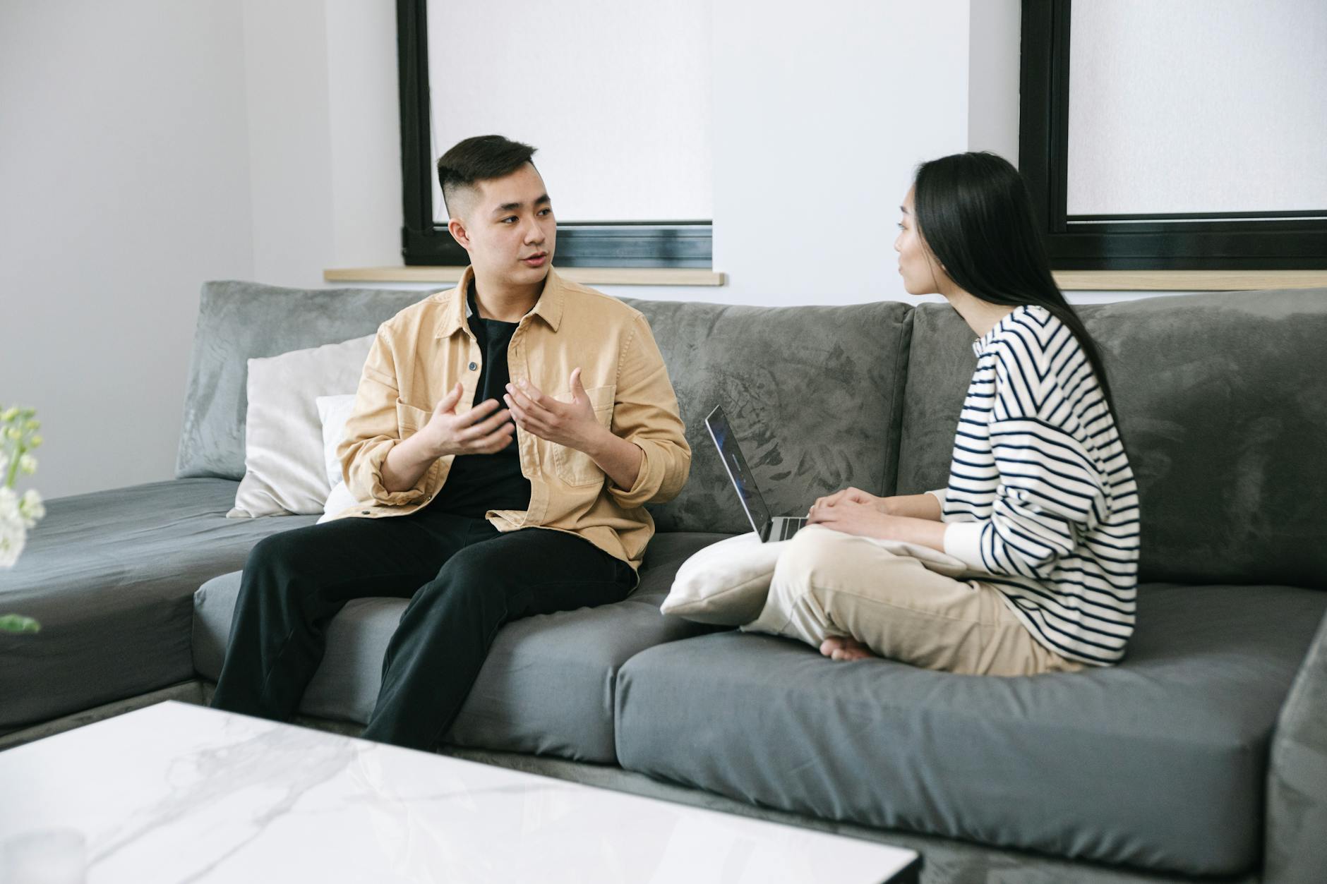 Two young adults engaged in a conversation, sitting on a couch at home. - healthy relationship communication