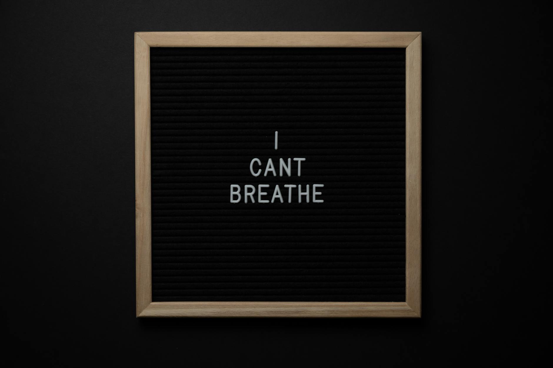 Top view of phrase I Cant Breath on small black signboard with light beige thin frame on black background - i feel statements