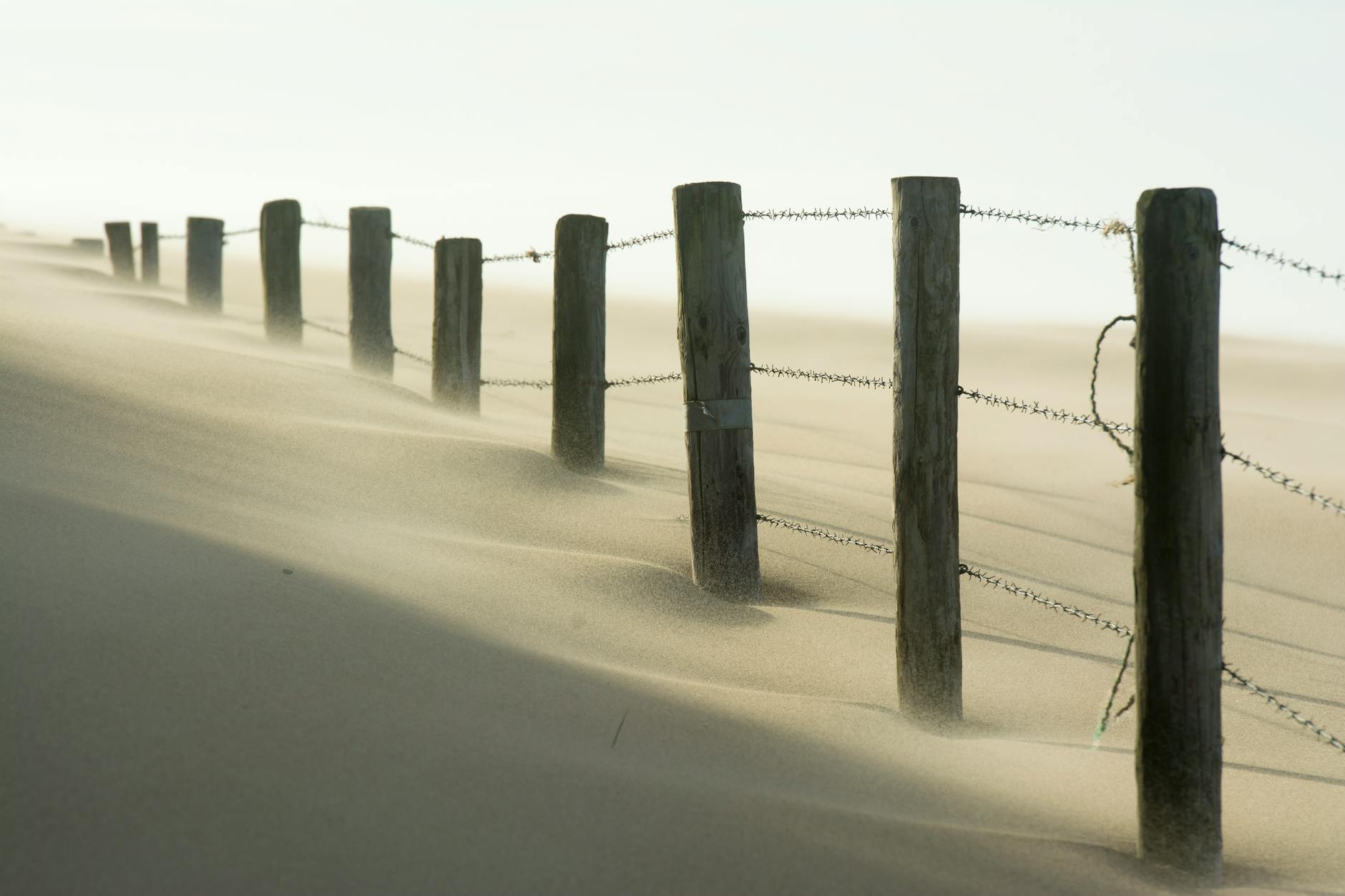 A scenic view of a barbed wire fence stretching across sandy dunes, with wind blowing sand. - in-law boundaries
