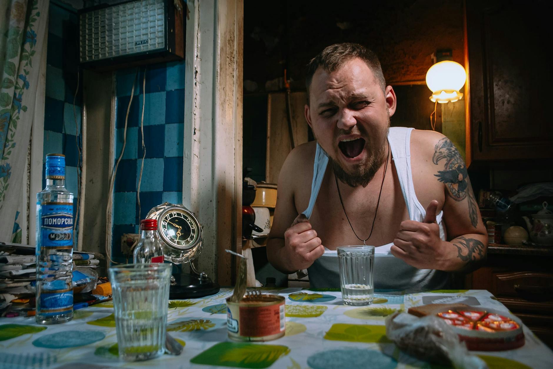 A man showing frustration in a dimly lit kitchen with scattered items including vodka and food. - journaling emotional release