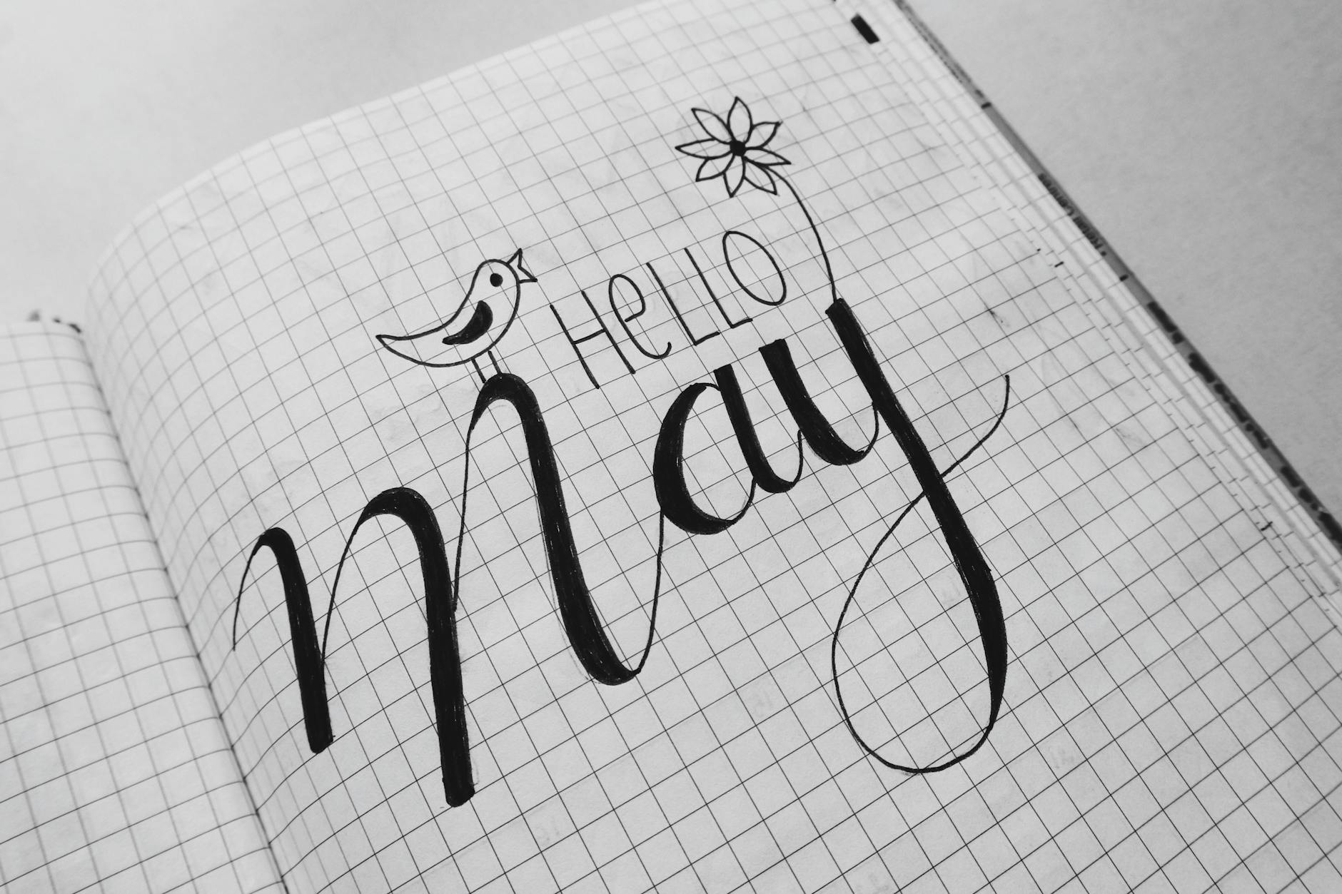 Black and white artistic calligraphy of 'Hello May' in a notebook with flower and bird doodles. - journaling emotional release