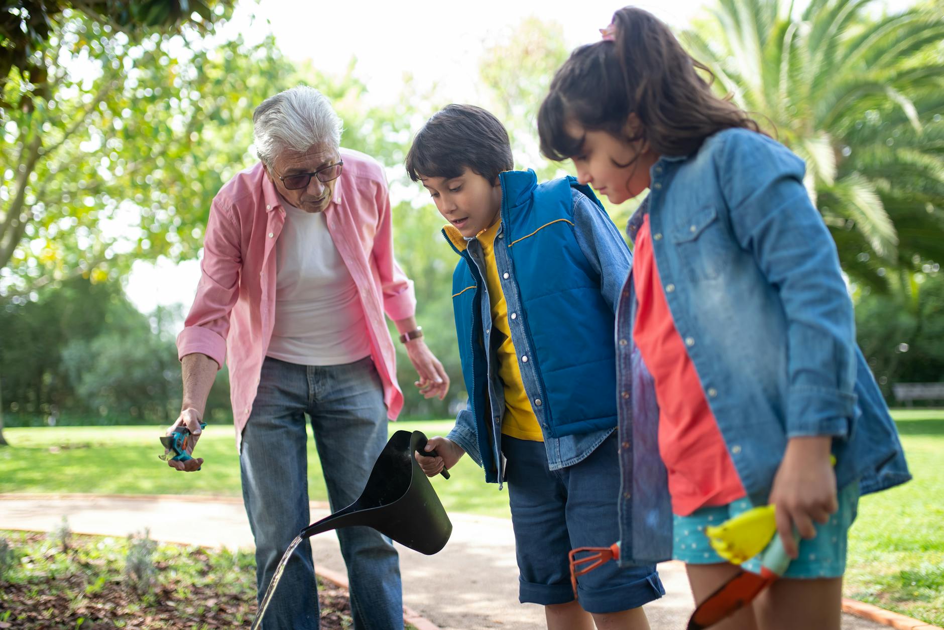 Elderly man gardening with his grandchildren in a sunny park. - kids spring gardening