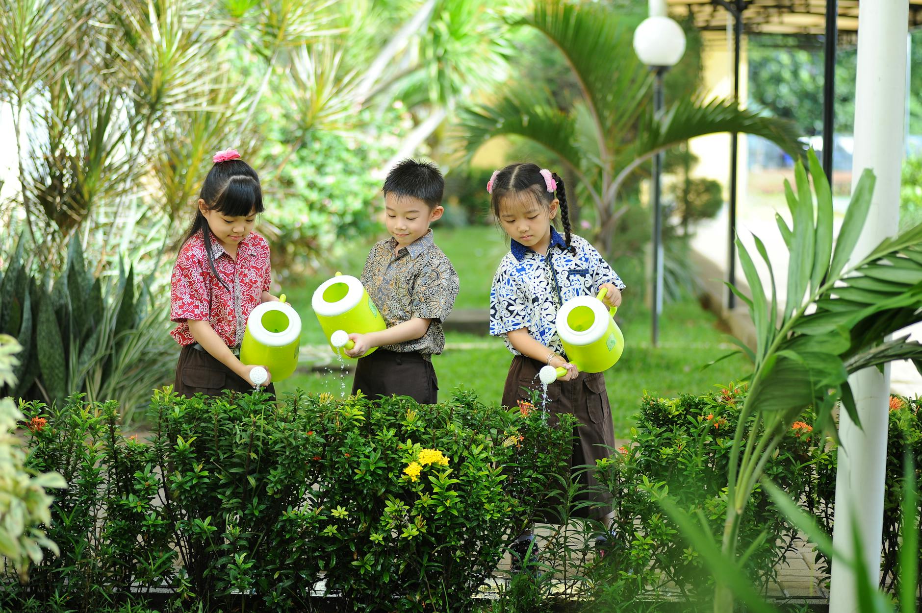 Three children in a garden watering plants with bright green watering cans, promoting teamwork and nature care. - kids spring gardening