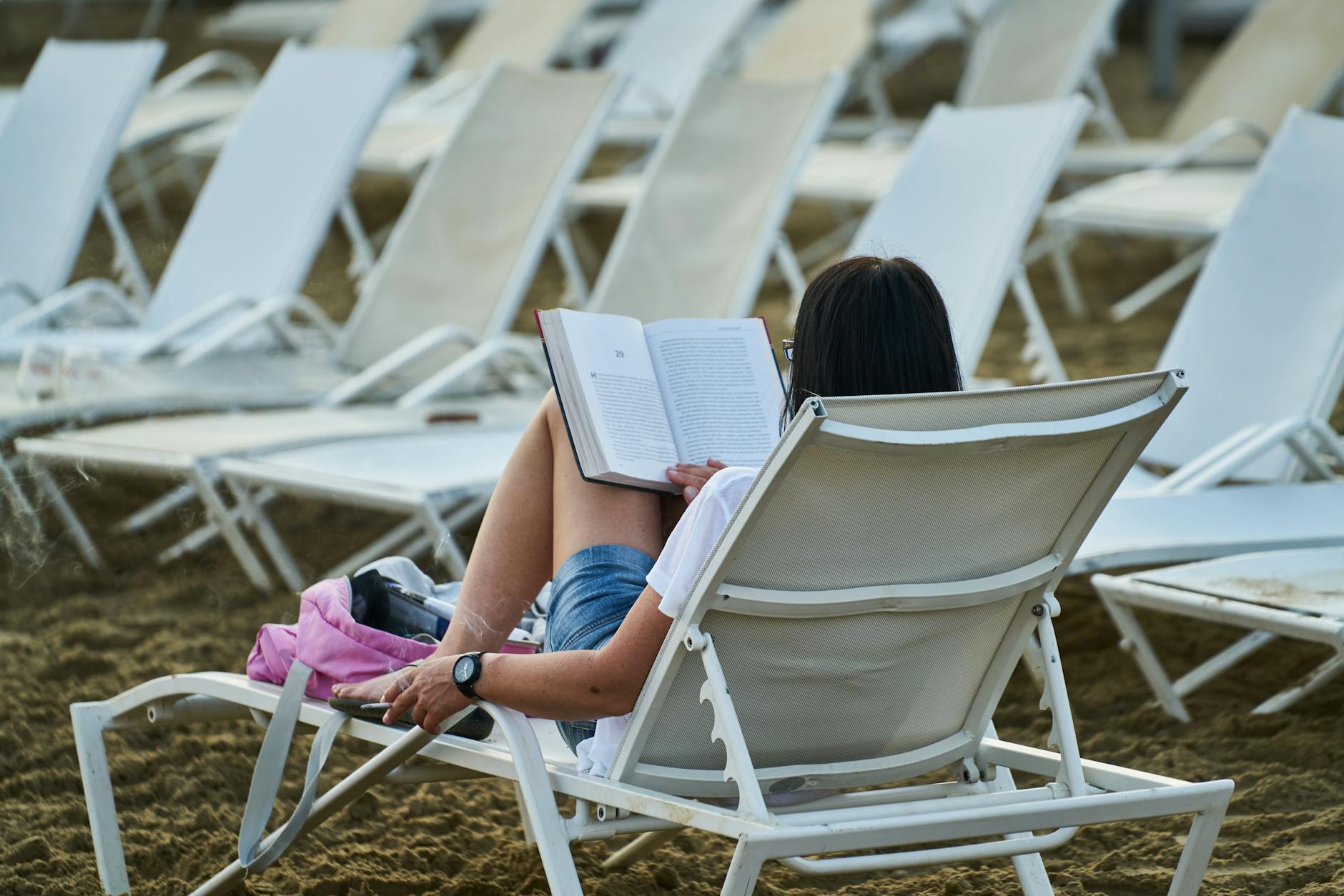 Woman reading a book on a lounge chair at the beach, enjoying a peaceful vacation day. - lack of empathy