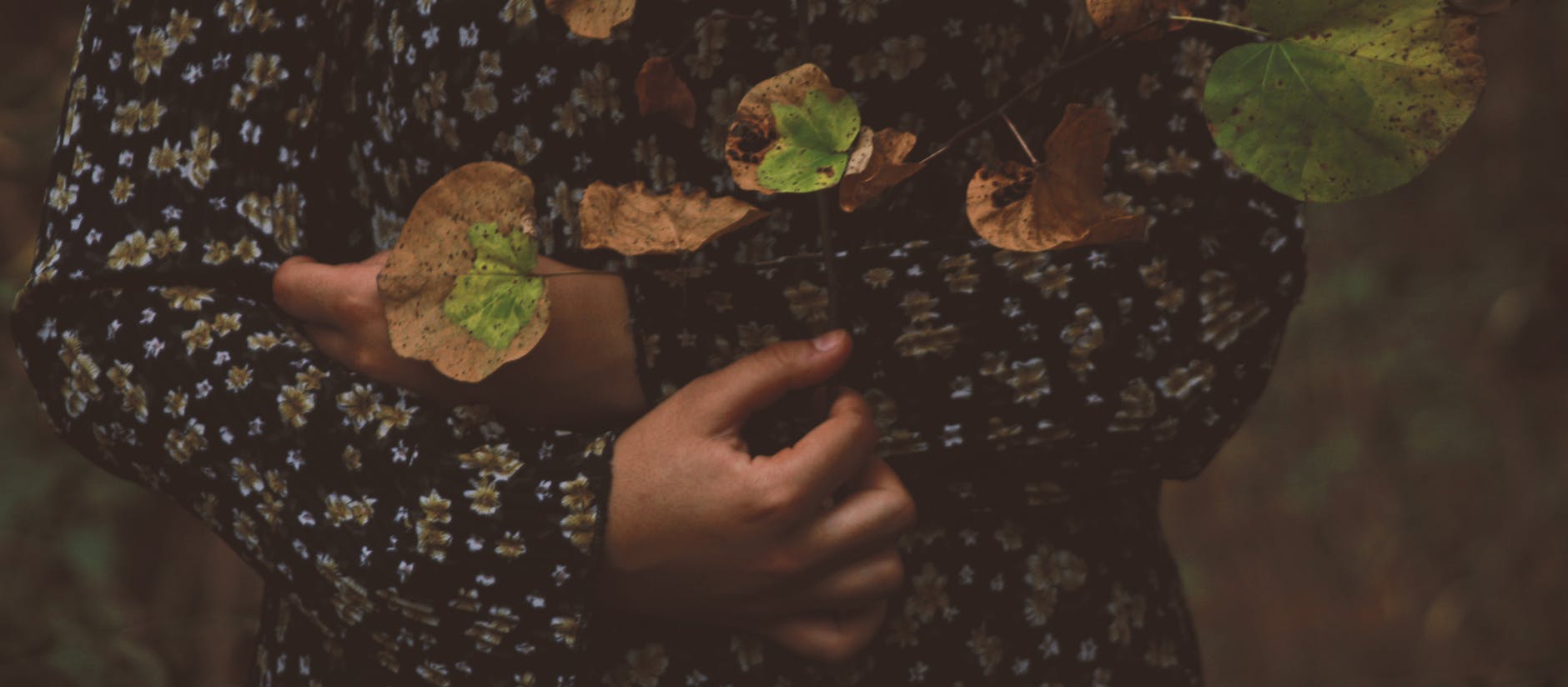 A woman embraces autumn leaves, showcasing a floral patterned dress in a moody setting. - let go of past hurts